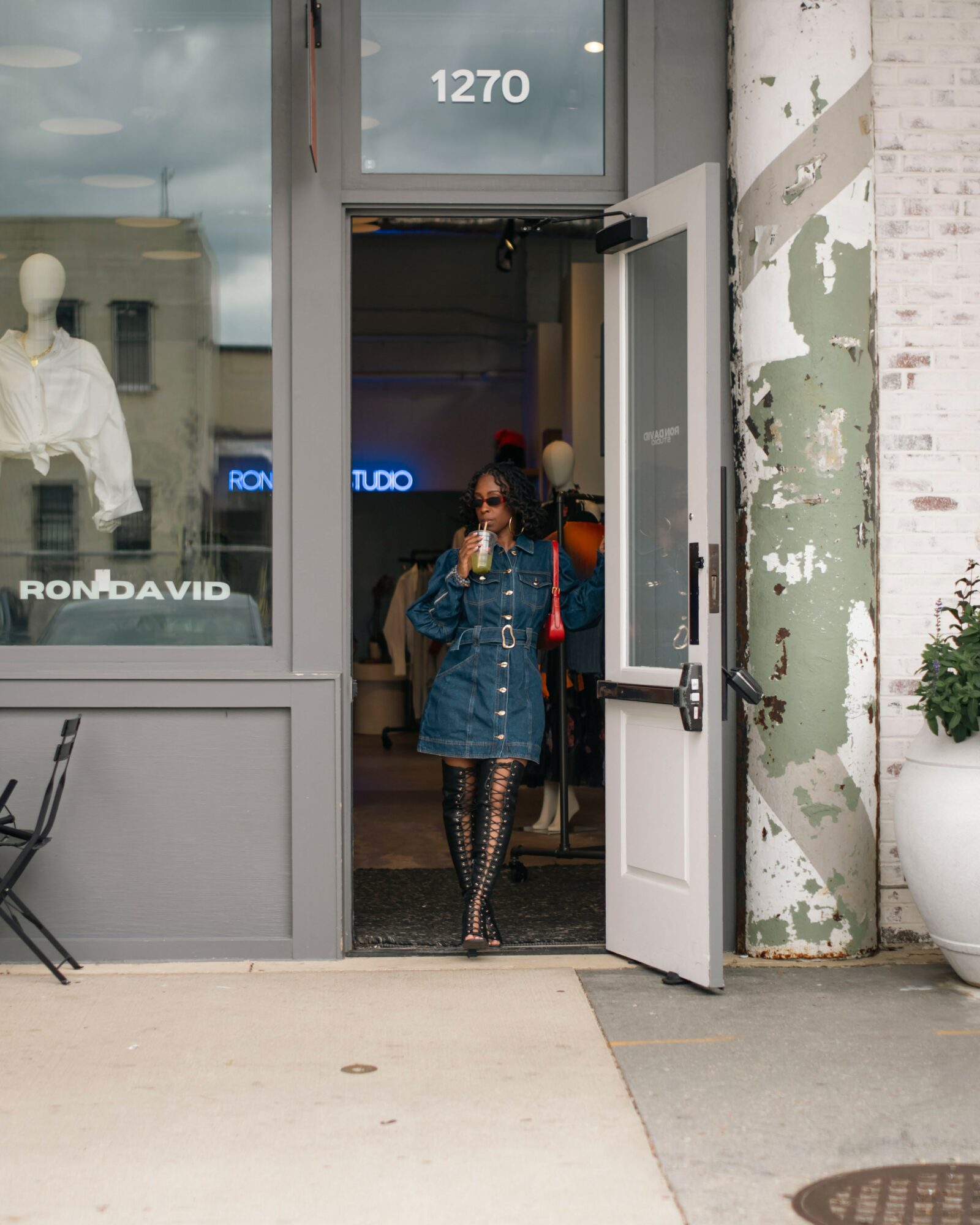 Woman in denim jacket and patterned tights exiting a store through a white door, with a mannequin visible inside.