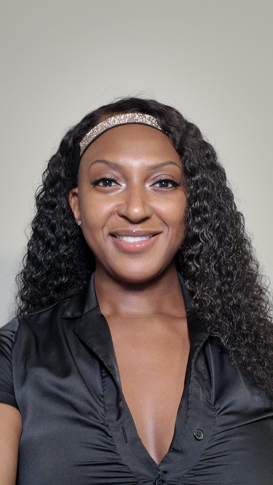 Woman with curly hair wearing a headband and black shirt, smiling, against a plain background.