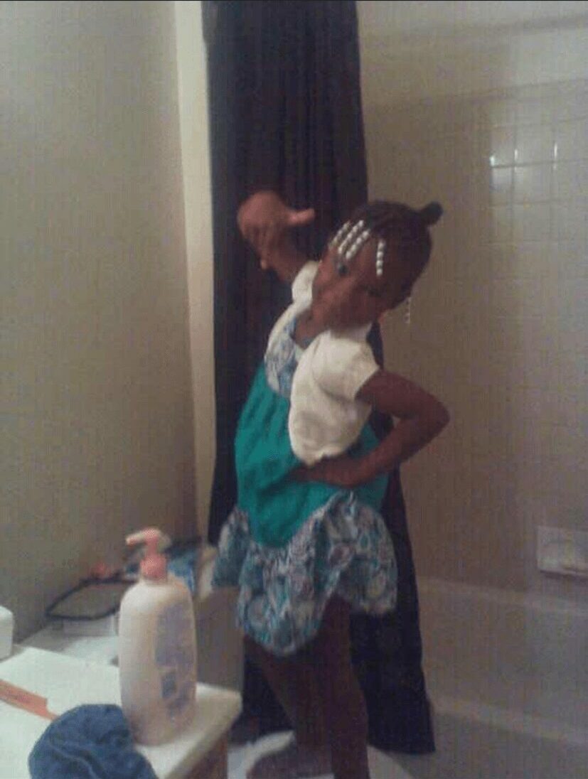 Two children taking a mirror selfie in a bathroom, one holding a phone, with a bottle on the counter nearby.