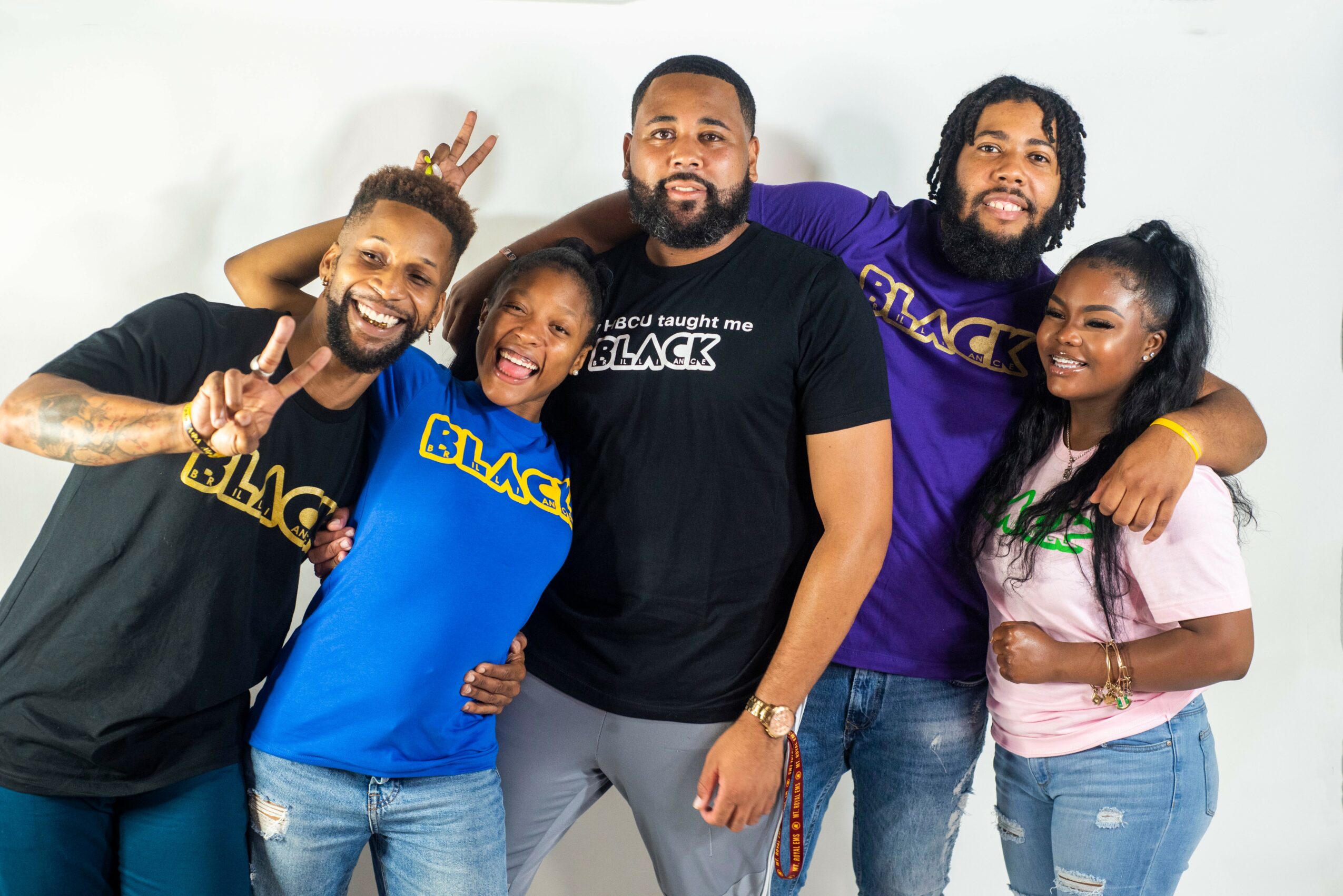 Group of five diverse people smiling, posing, and making peace signs, standing together against a white background.