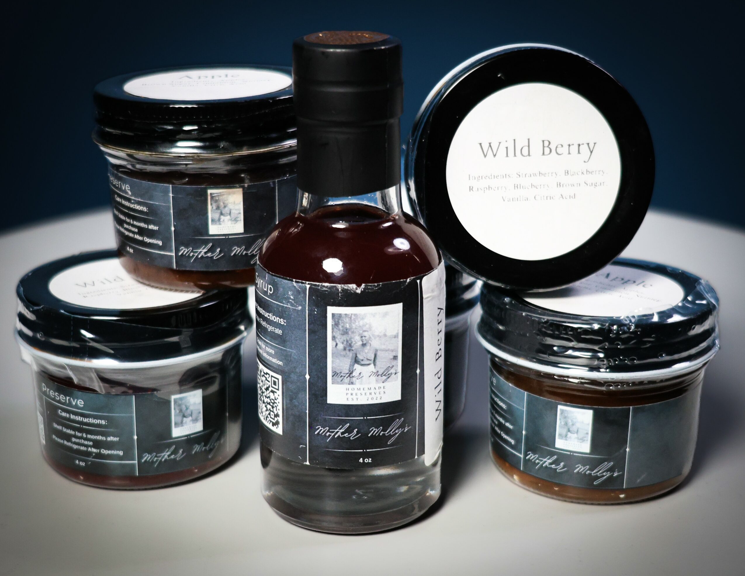 Assorted jars and a bottle of dark liquid with labels, arranged on a surface against a dark background.