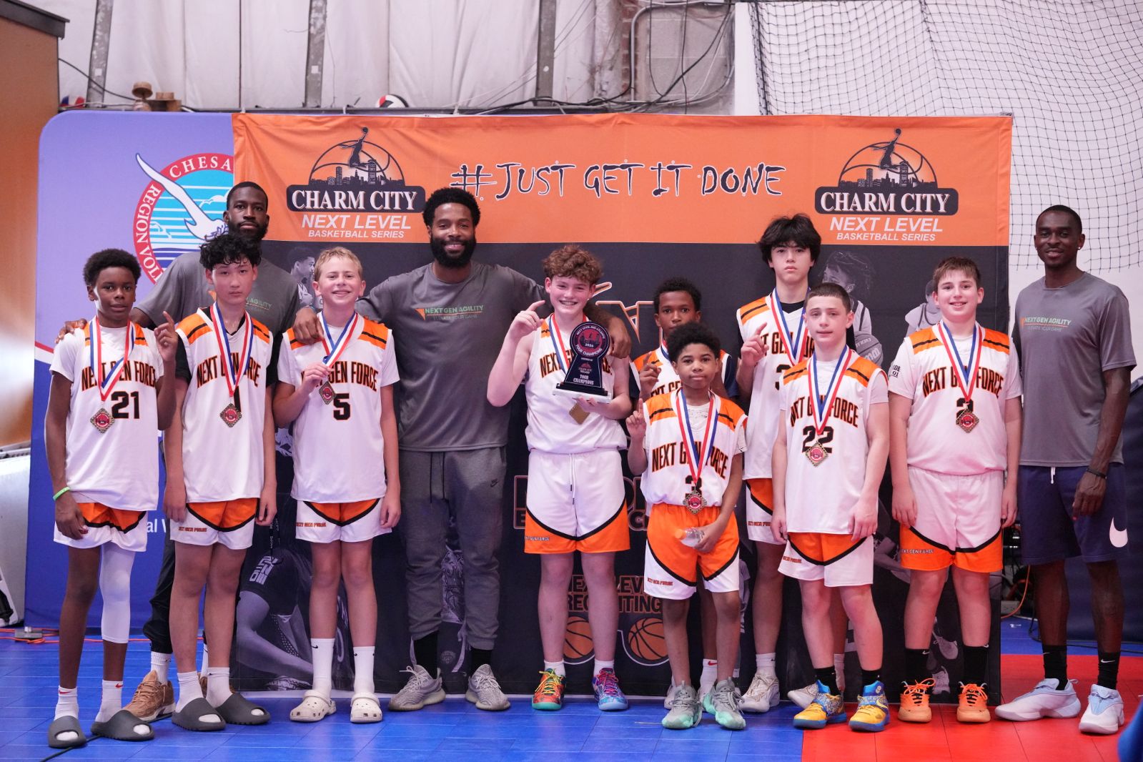 Group of young basketball players with medals, coaches, and a banner in the background, celebrating victory.