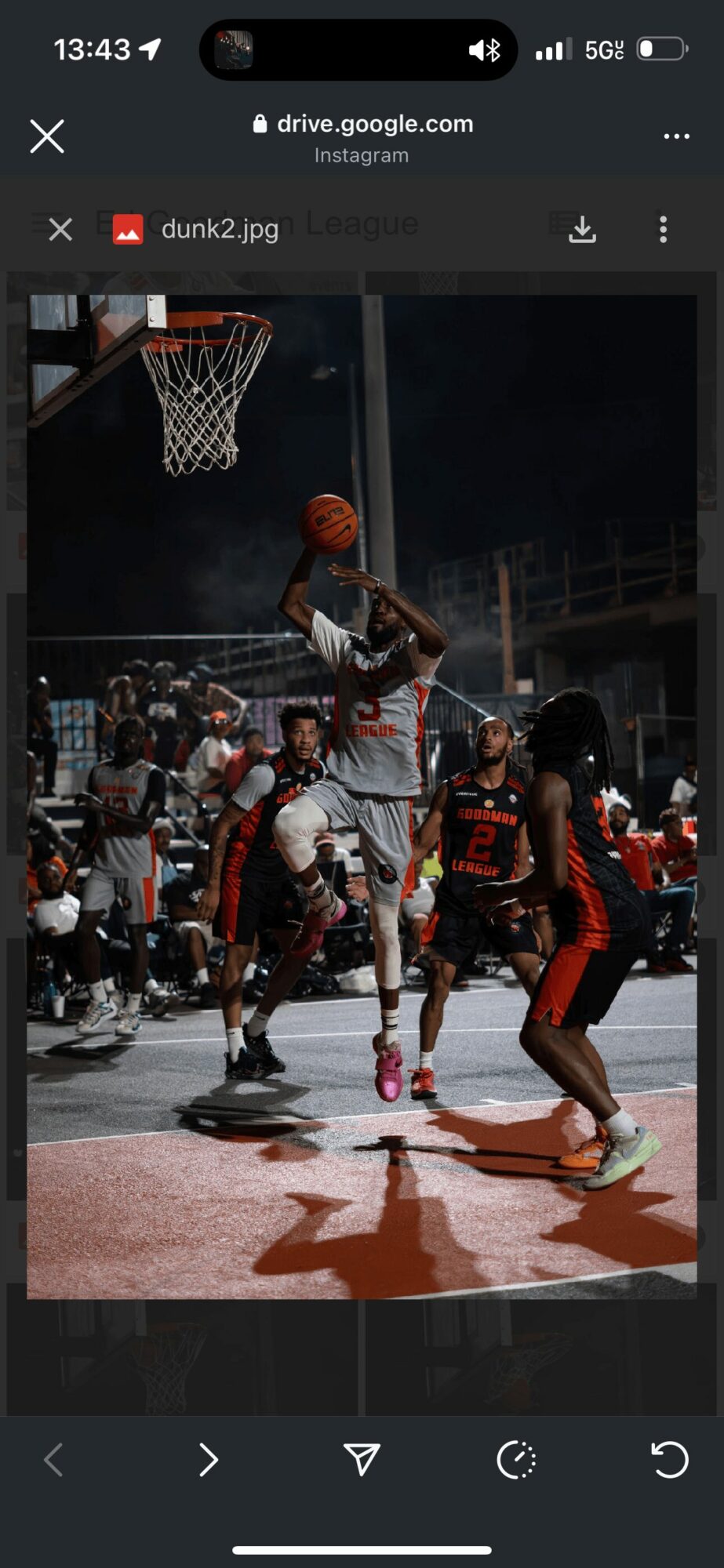 A basketball player with a prosthetic leg jumps to shoot, surrounded by defenders on an outdoor court at night.