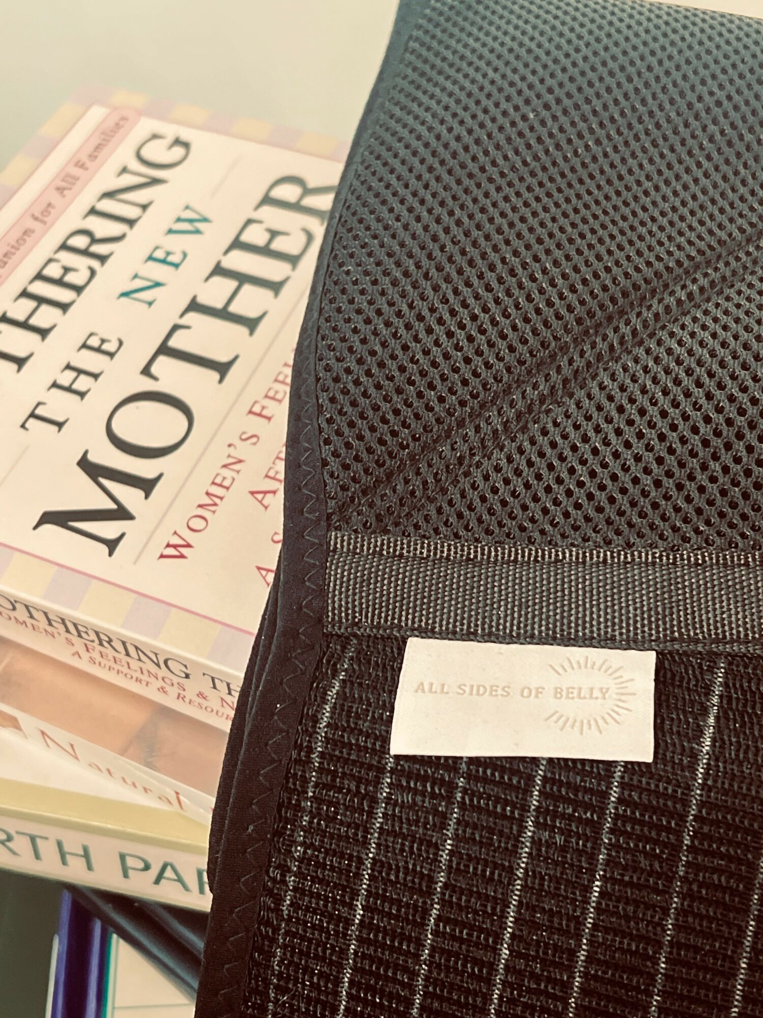 Part of a book titled 'The New Mother' and a black fabric item with a label, on a surface.