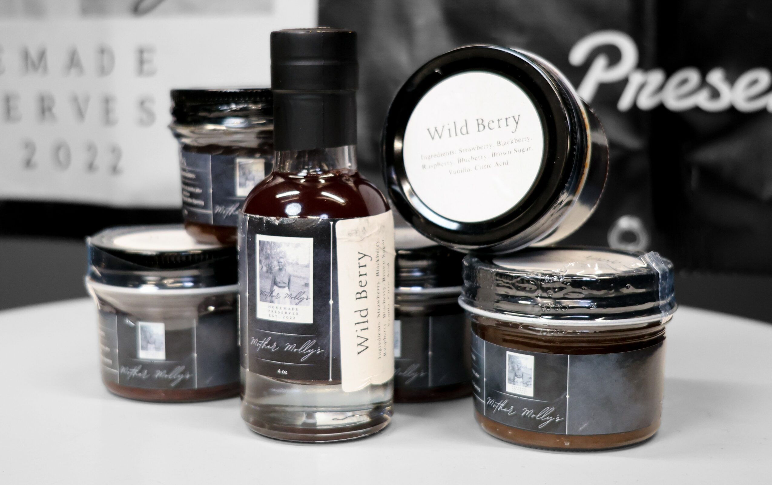 Collection of jars and a bottle with labels, displayed on a white surface, with a blurred background.