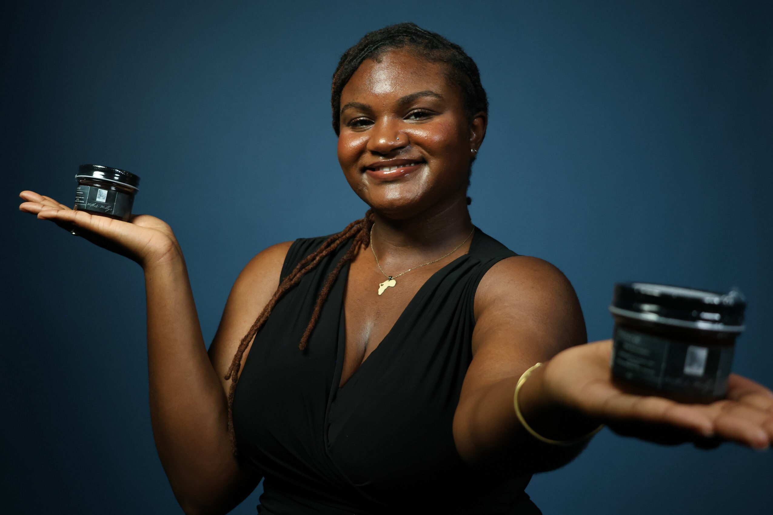 Smiling woman holding two small containers, one in each hand, against a blue background.