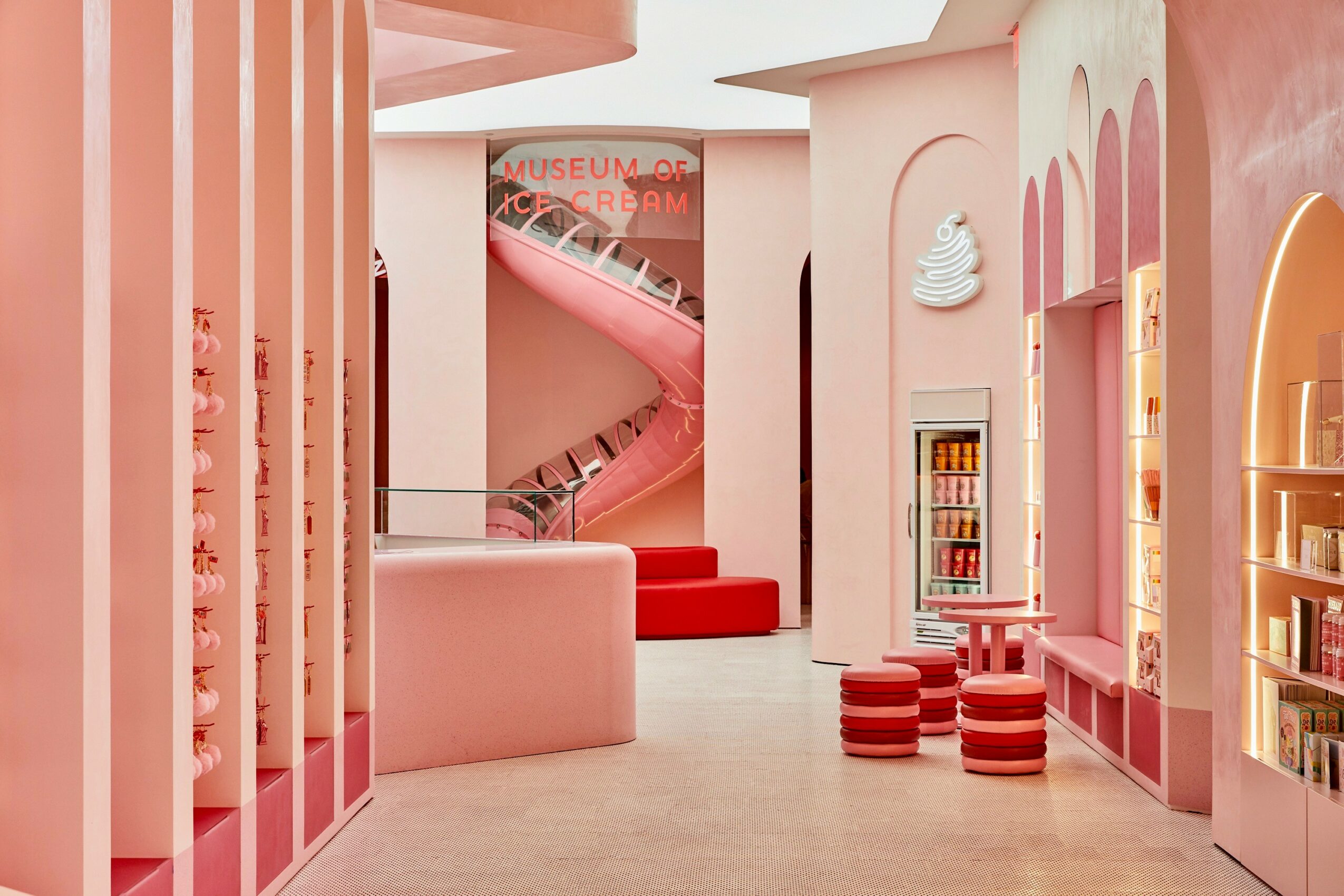 Interior of a museum with pink and white decor, spiral staircase, and display shelves, bright and inviting atmosphere.