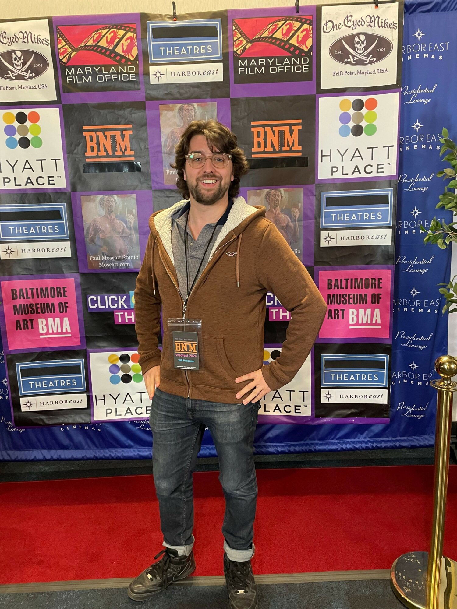 Person standing in front of a colorful display of posters and books, wearing a brown jacket and jeans.