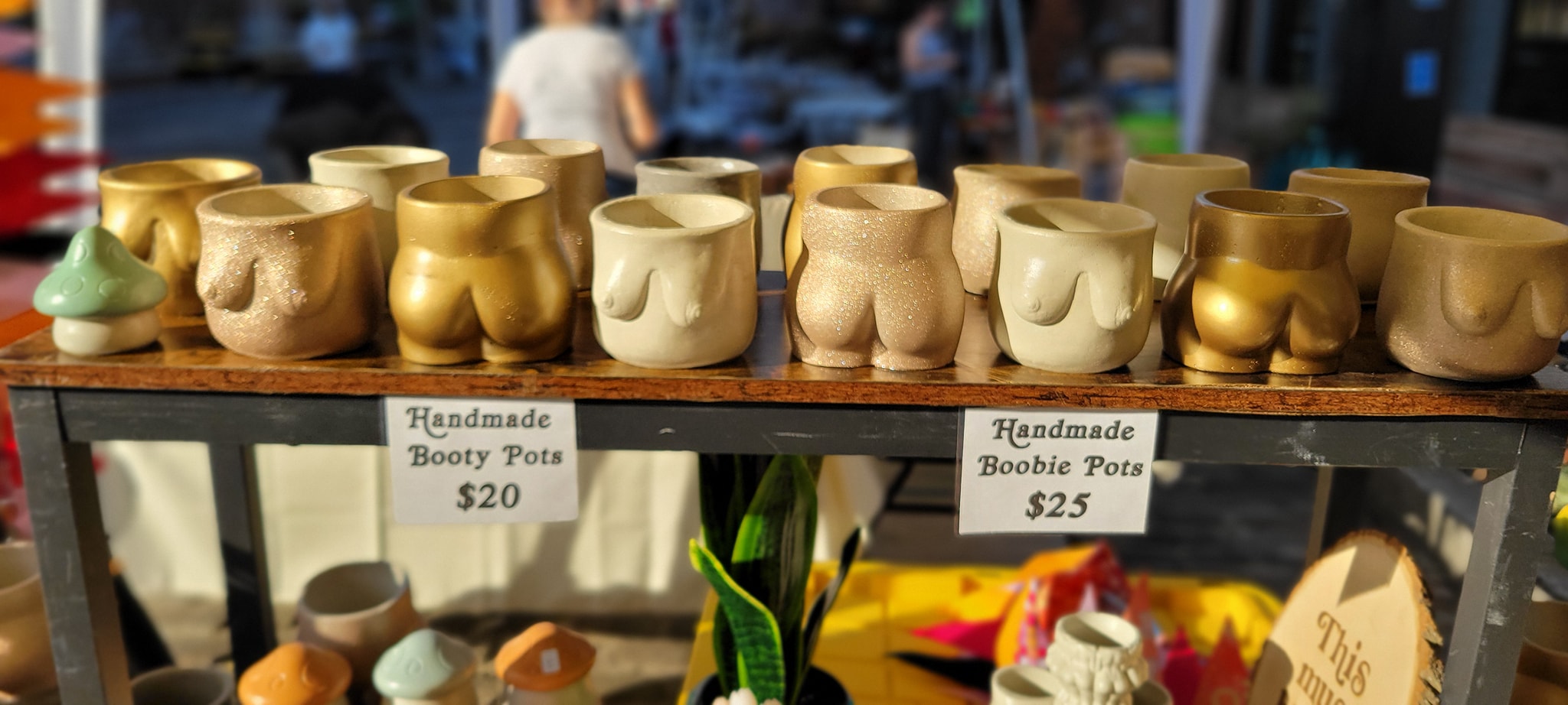Display of handmade pottery in various shapes and colors on a table at an outdoor market, with people in the background.