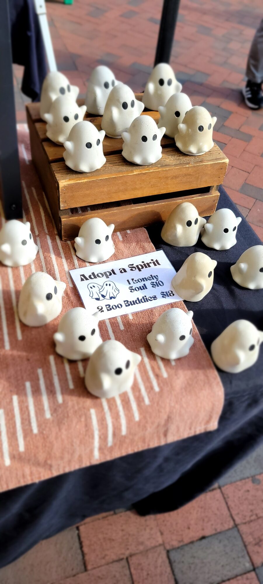 Small white bunny figurines on a table with a sign about adopting a bunny, some on a wooden stand, others scattered.