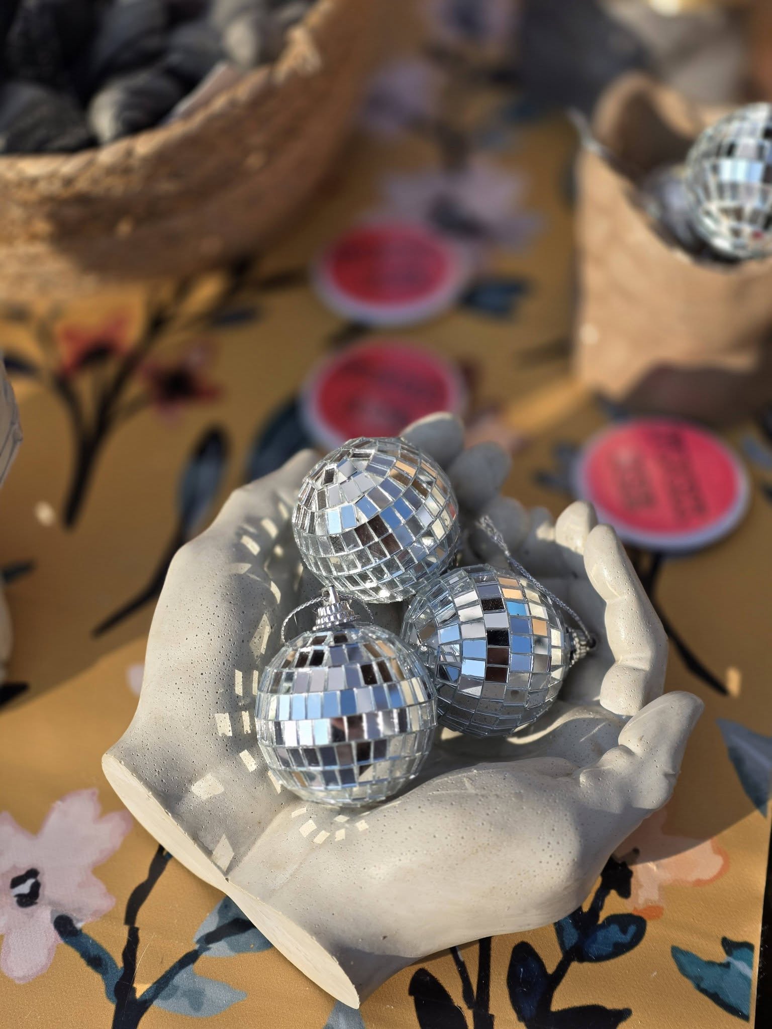 Four small disco ball ornaments in a white paper bowl on a colorful tablecloth with pink circular labels.