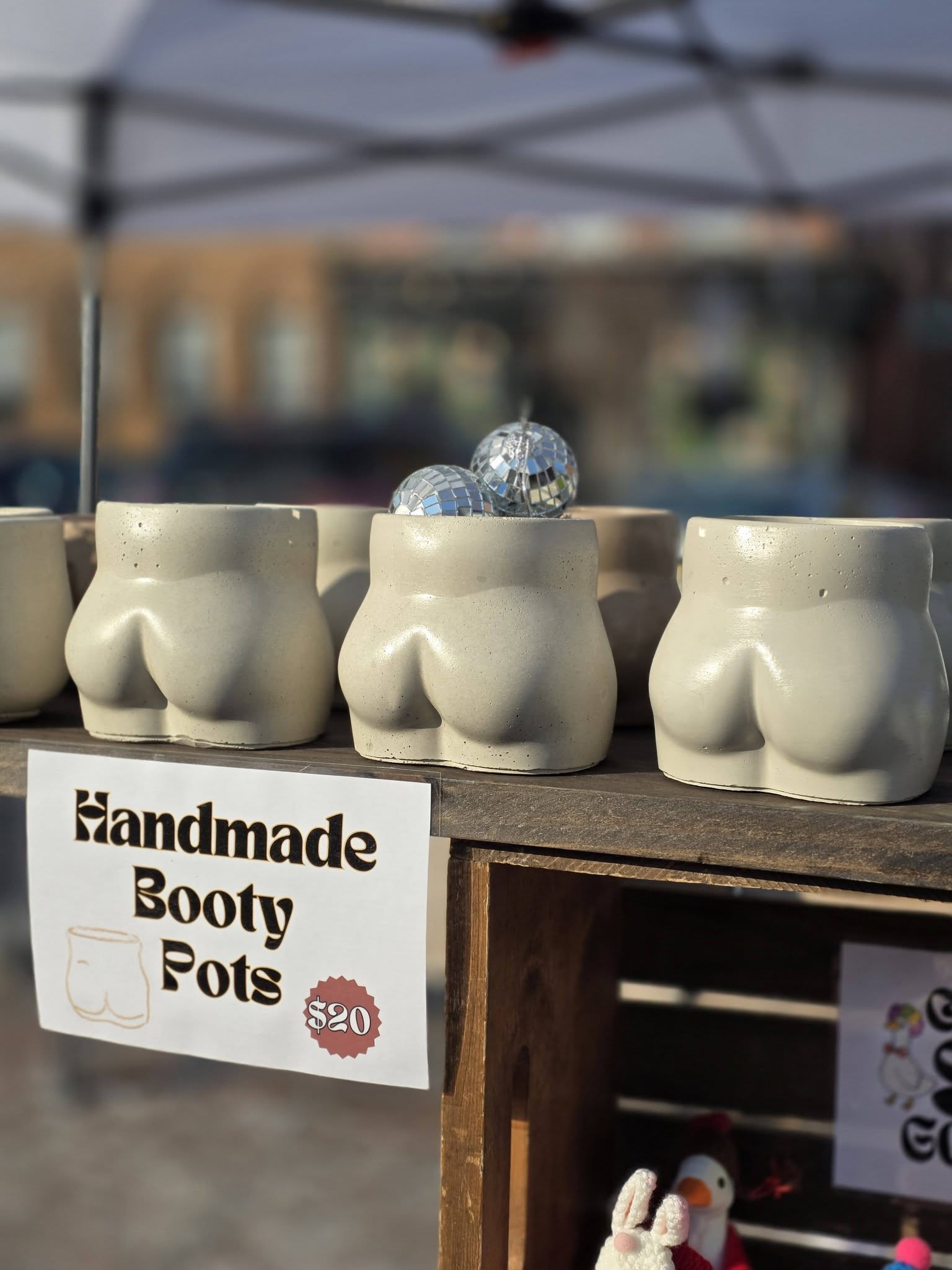Three handmade boot-shaped pots with shiny decorative balls on top, displayed outdoors under a canopy, with a sign advertising for $20.