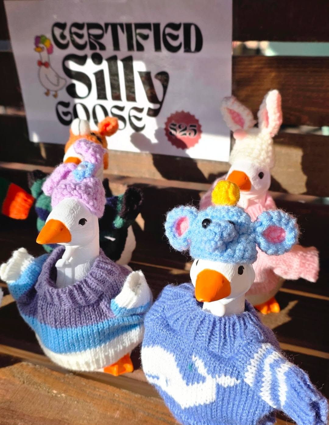 Four plush animal toys dressed in knitted sweaters, with a sign behind them reading 