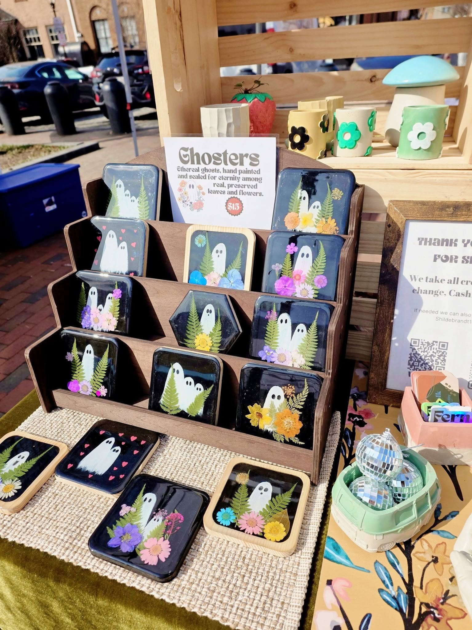 Display of ghost-themed pins and accessories on a table with wooden backdrop, including small trays and decorative items.