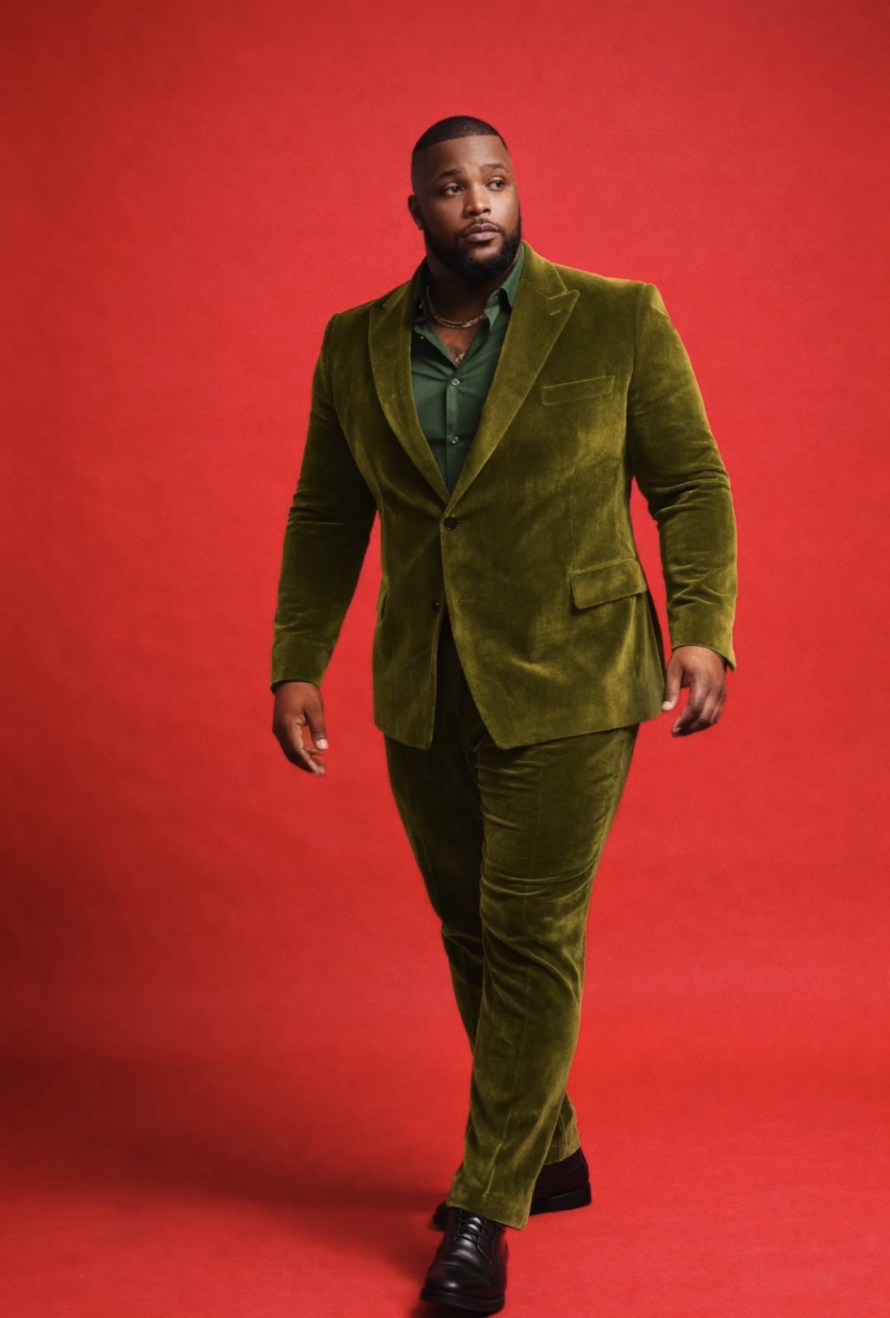 Man in a green velvet suit walking against a red background.