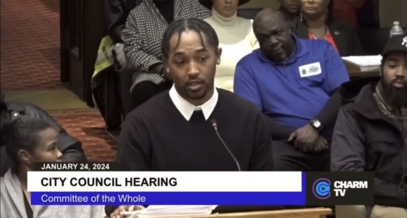 Man speaking at city council hearing with audience in background, January 24, 2024, Charm TV logo, committee of the whole.