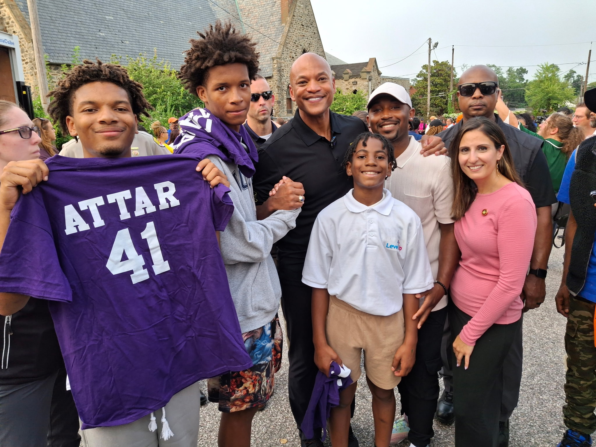 Group of people smiling outdoors, some holding a purple sports jersey with 'ATTAR 41'.