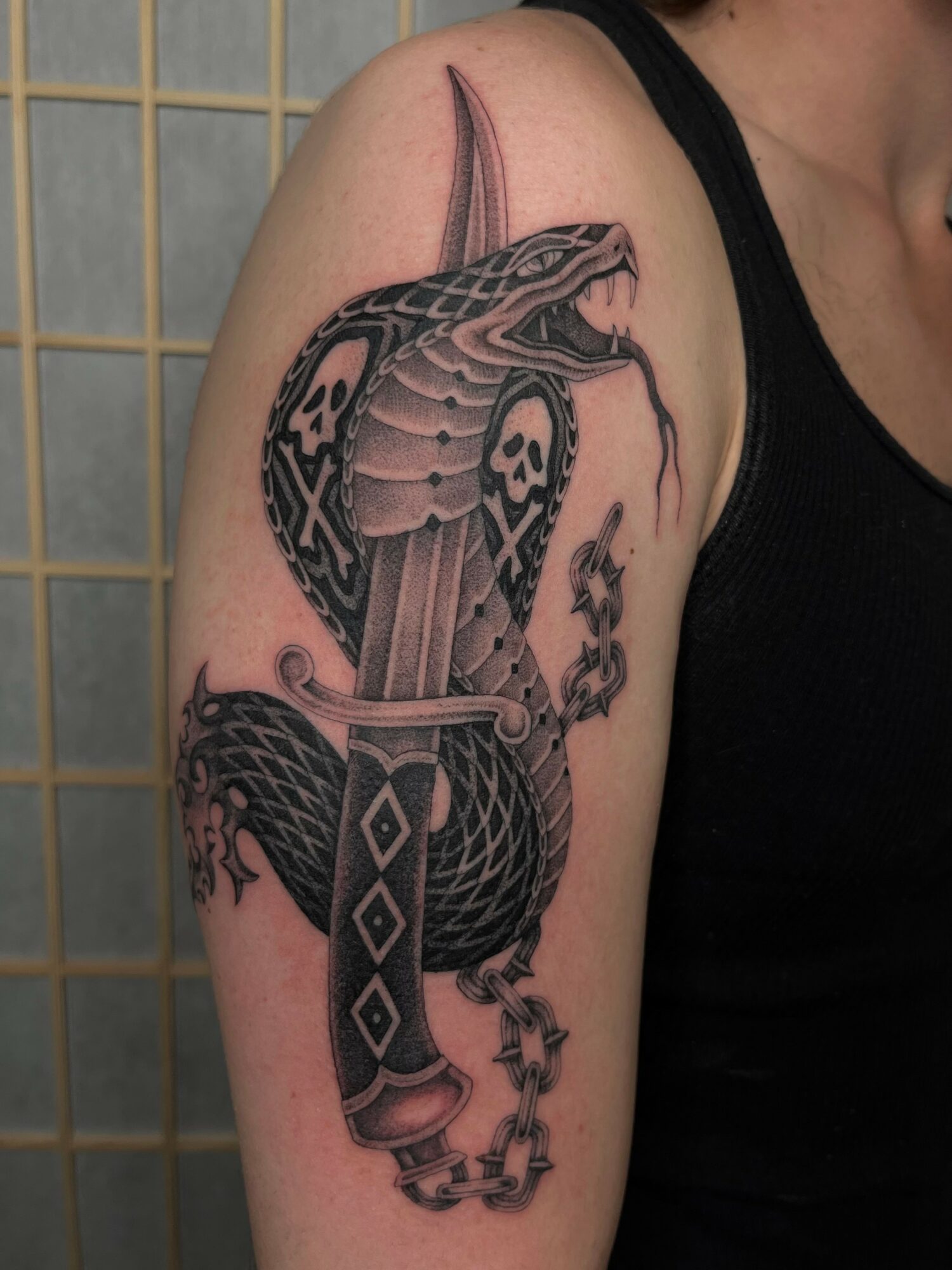 Tattoo of a snake coiled around a sword on a person's upper arm, with detailed scales and shading.