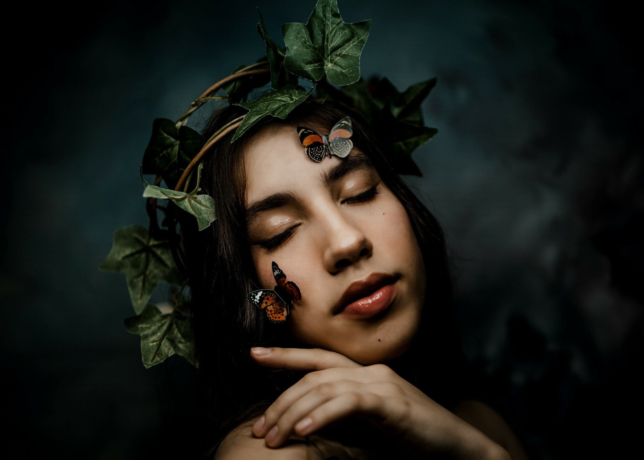 Woman with closed eyes, wearing a leafy crown, surrounded by butterflies, in a dark, moody setting.