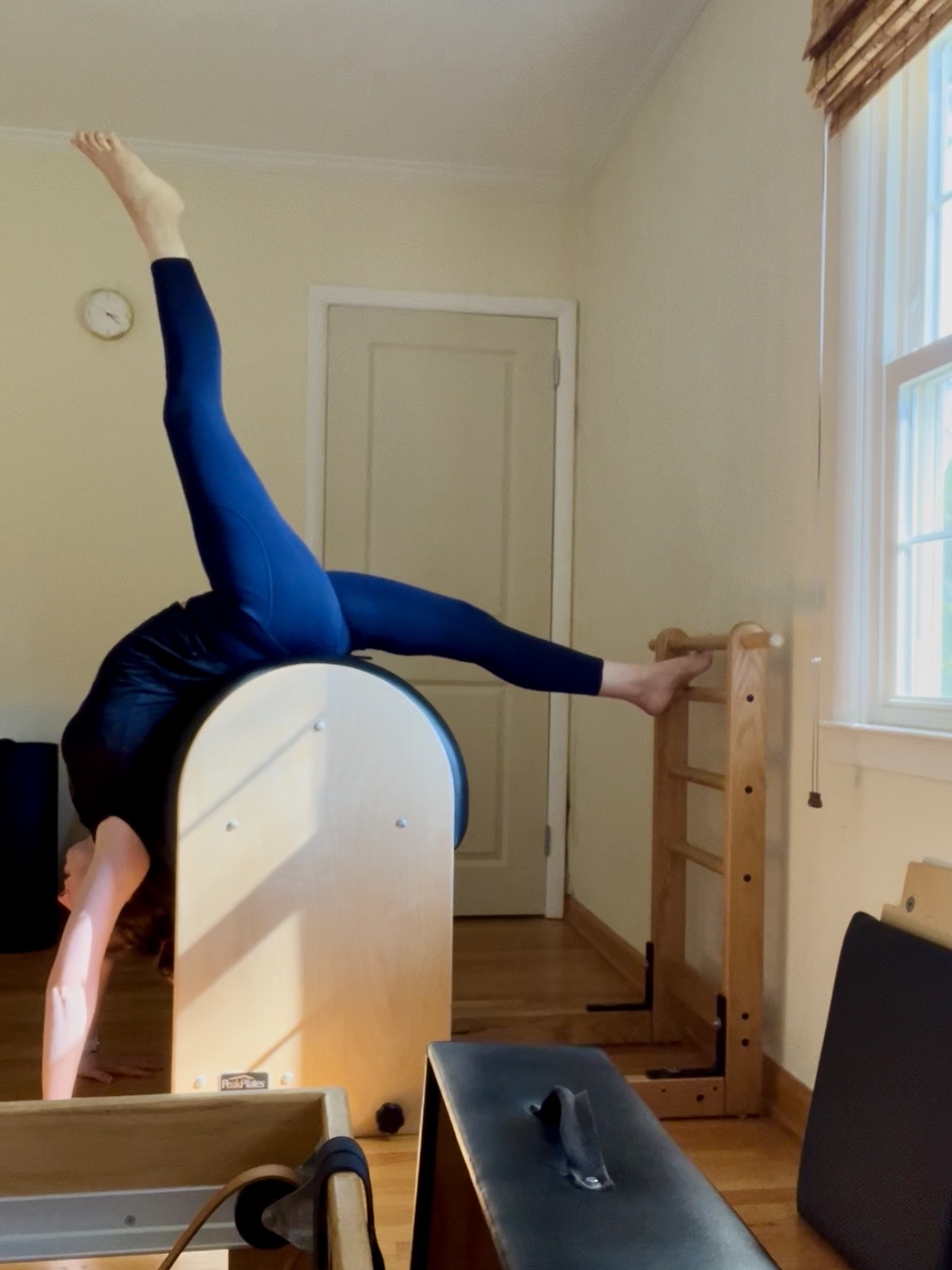 Person performing a backbend with legs on a wooden structure in a room with a window and door, facing downward.