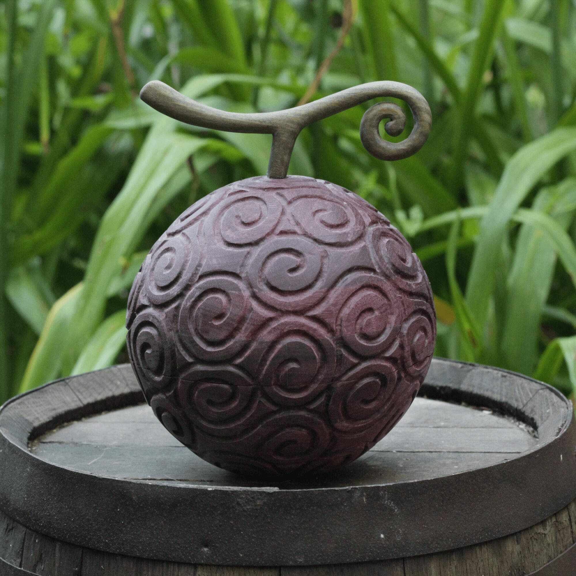 Decorative spherical object with swirling patterns and a curved handle on top, placed on a round surface outdoors.