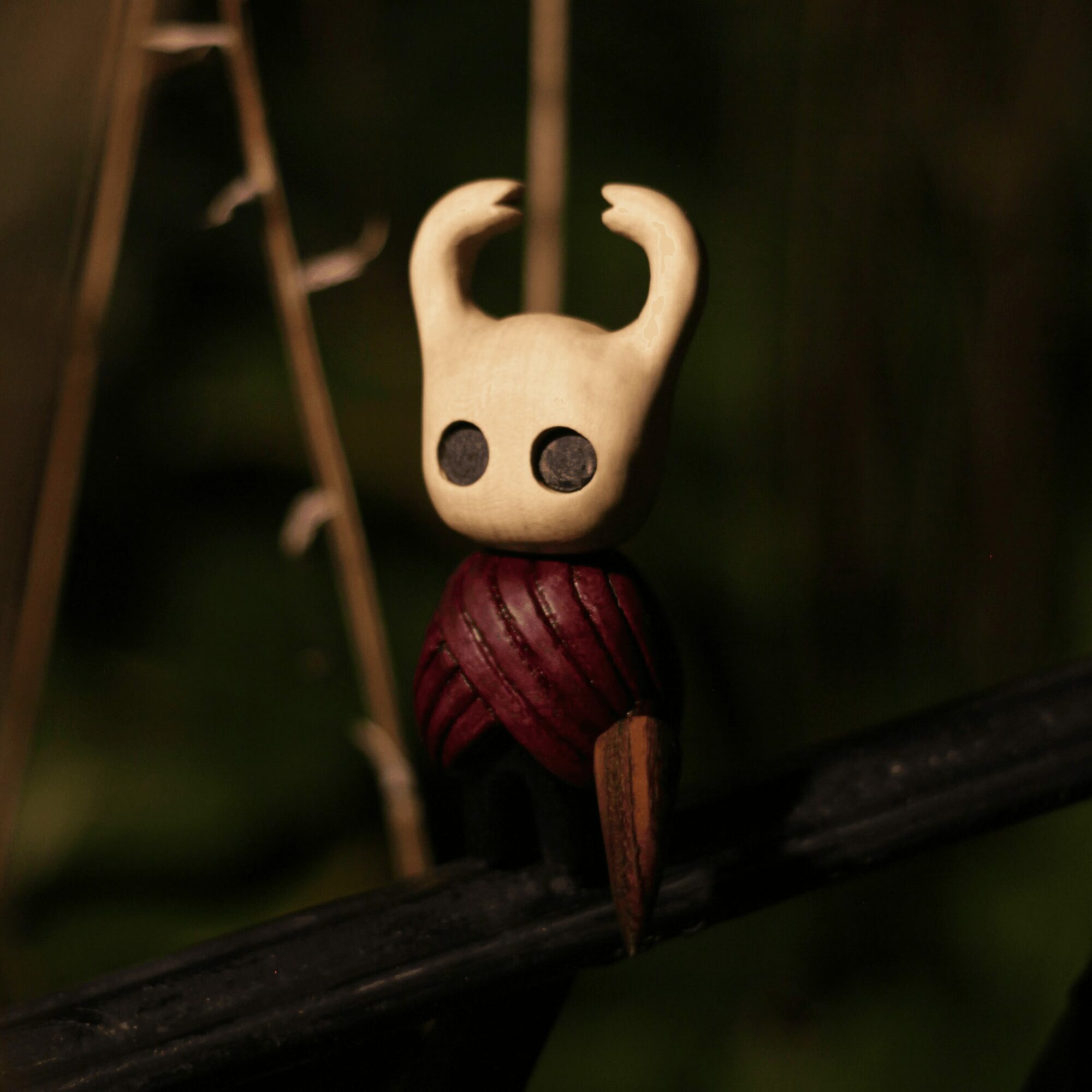 Small figurine with a cream-colored head, black eyes, and curved horns, sitting on a dark branch in a natural setting.