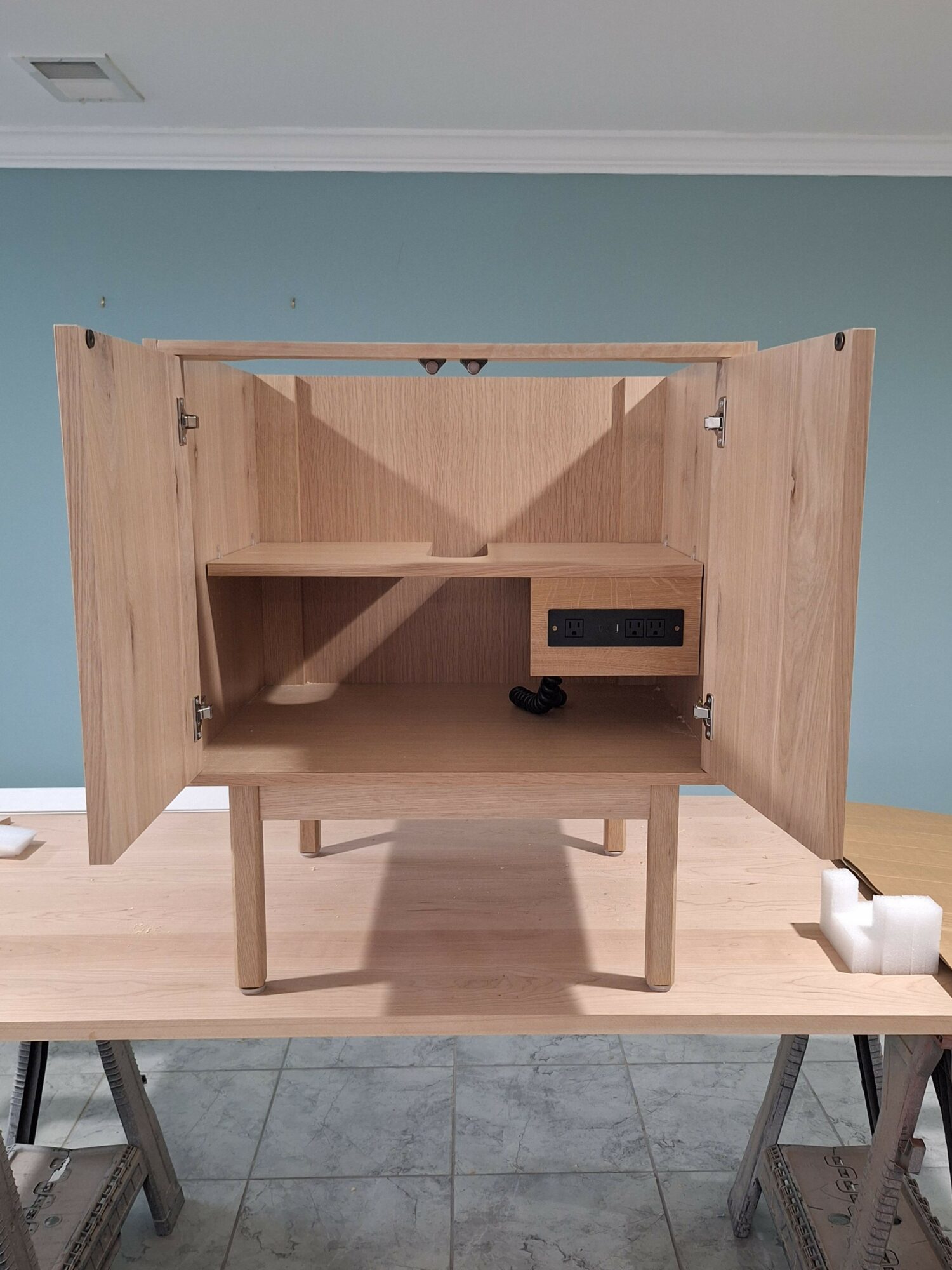 Wooden desk with open compartments and a chair, on a tiled floor, viewed from the side.