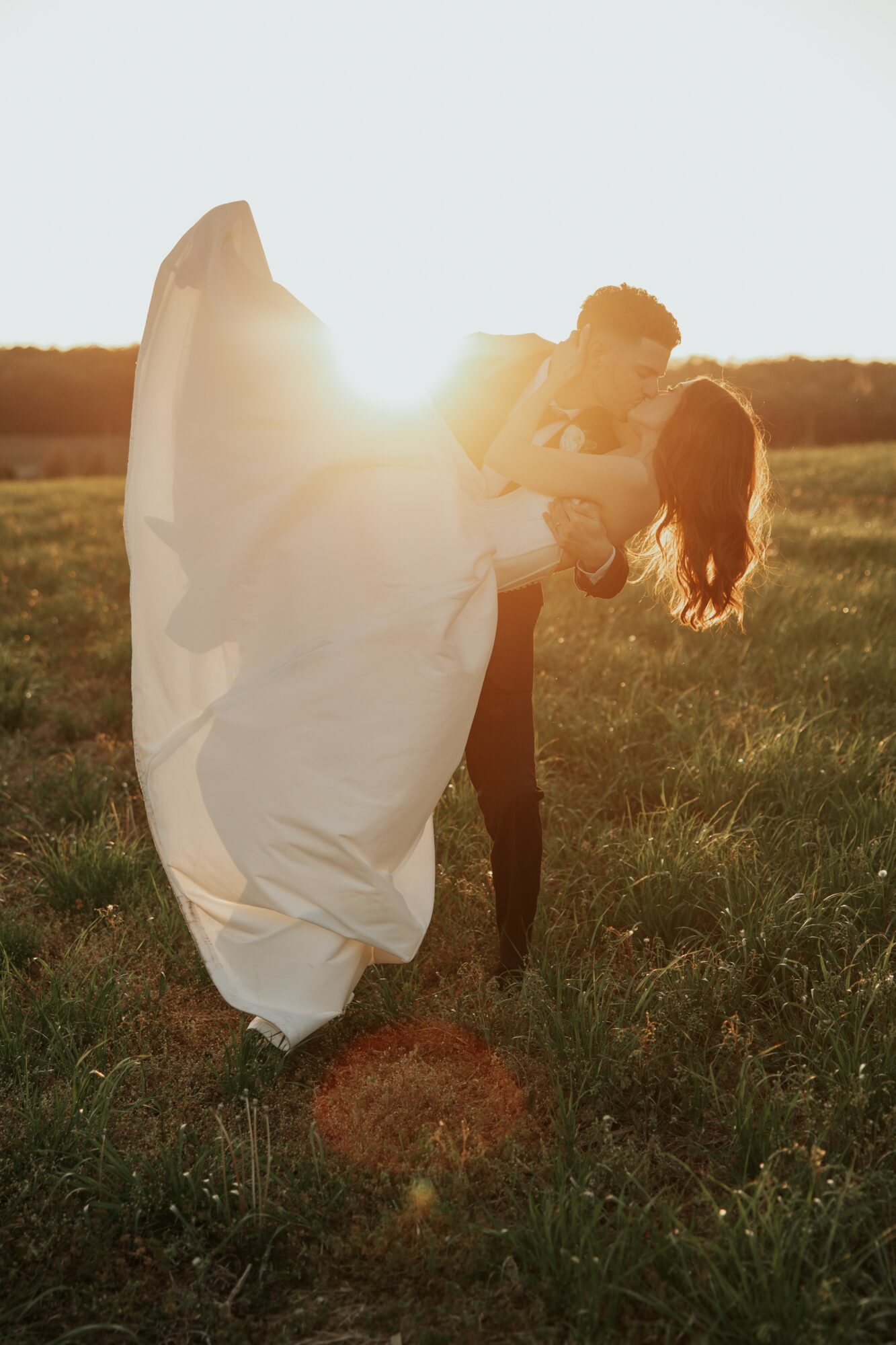 Person holding a child in a field during sunset, with the child’s hair and dress flowing in the wind.
