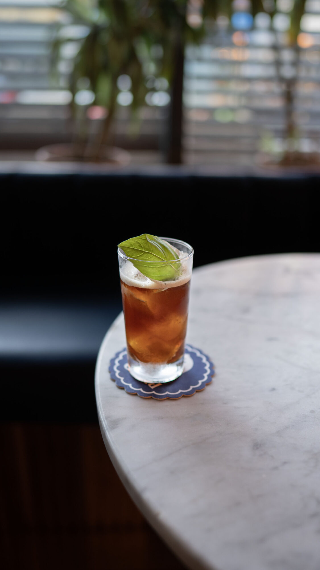 A glass of iced tea with a lime wedge on top, placed on a marble table with a blurred background.