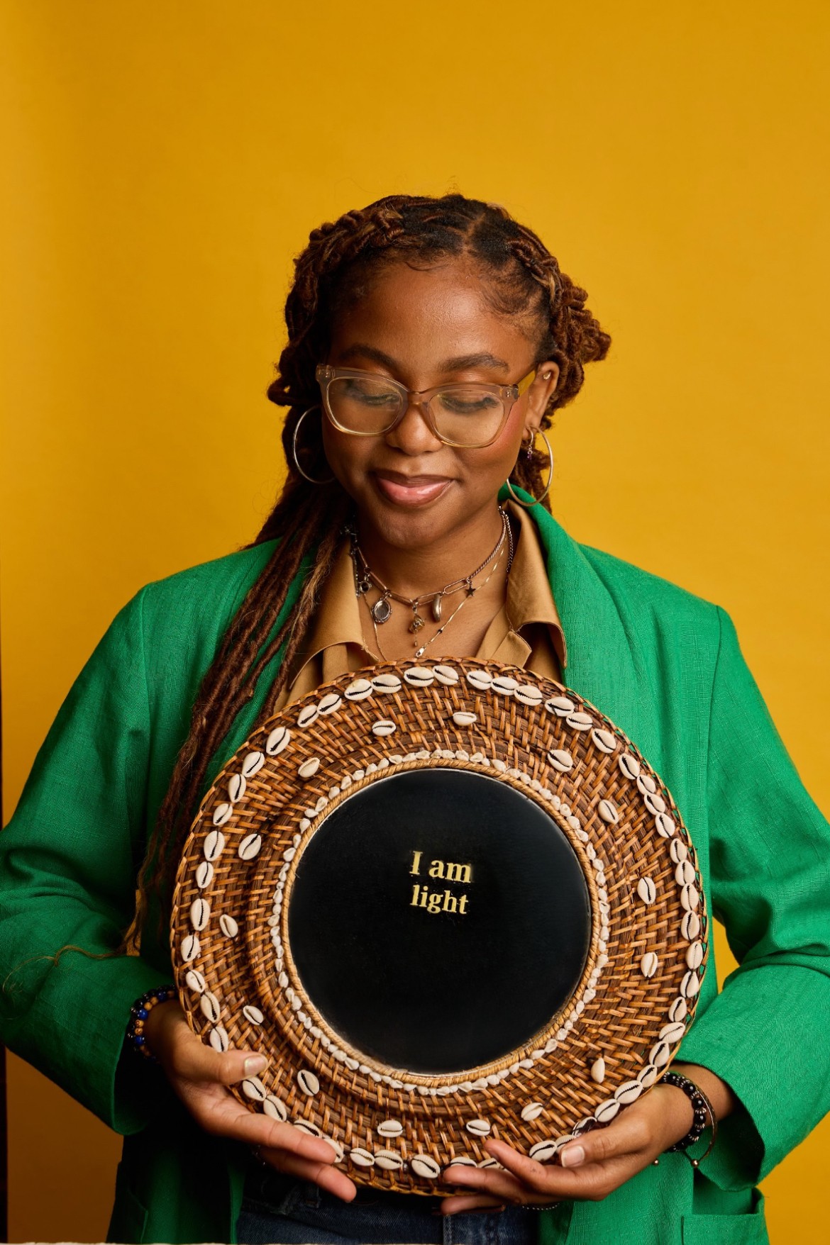 Woman with glasses and braided hair holding a circular object with text, against a yellow background.
