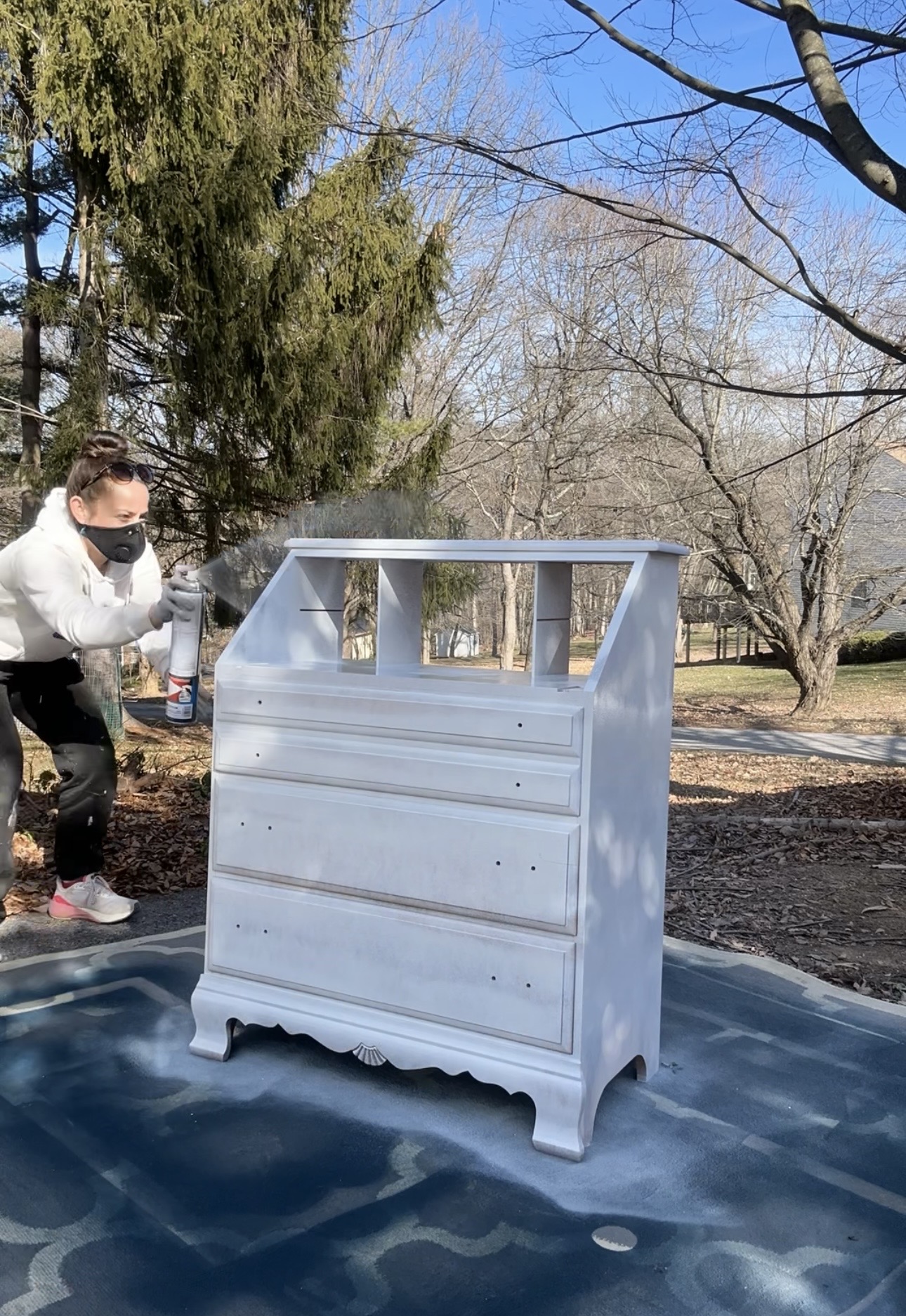 White dresser outdoors on a blue surface with trees and a person wearing a mask nearby.