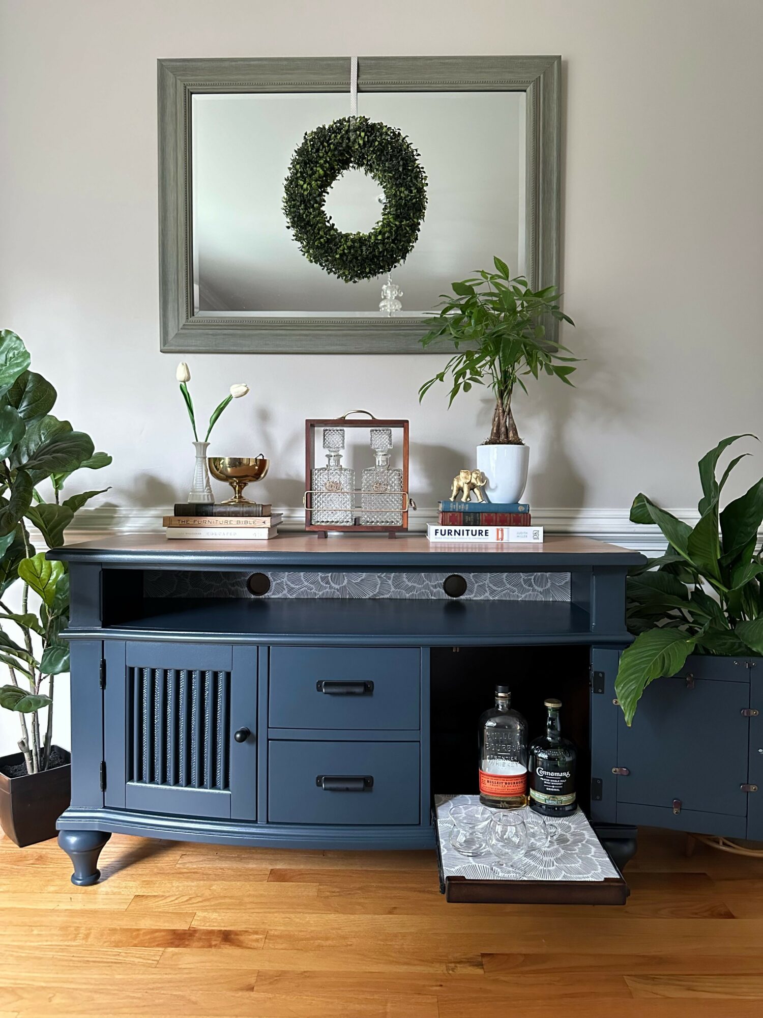 Blue sideboard with plants, bottles, and decorative items in a room with wooden floor.