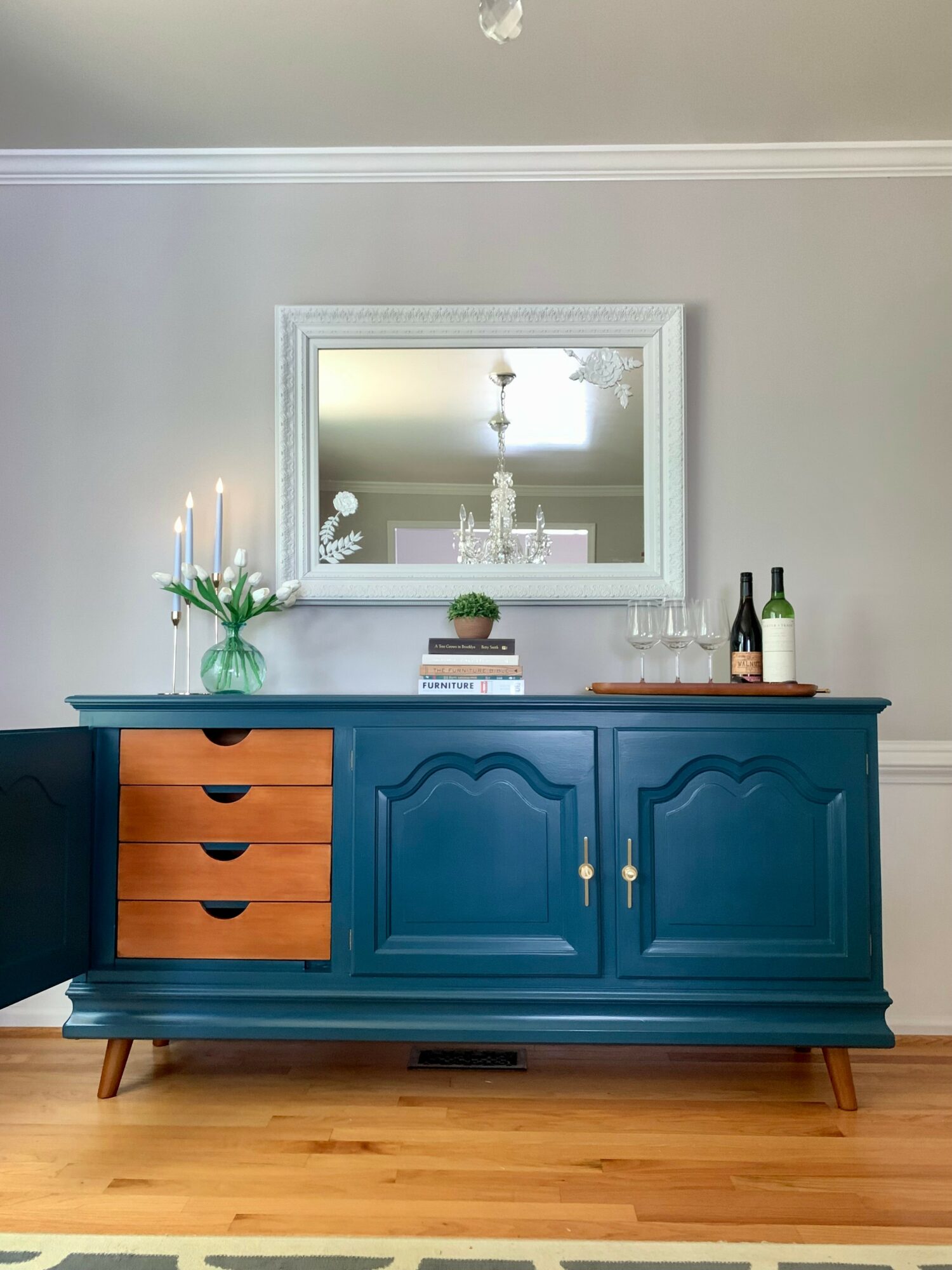 Blue sideboard with wooden drawers, a mirror above, and decorative items including a vase with flowers and bottles.