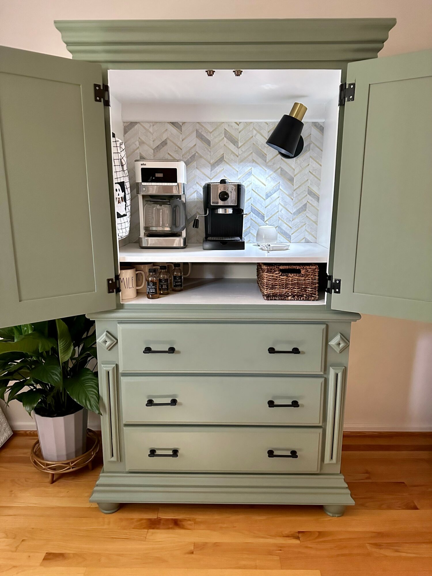 Open light green cabinet with drawers, kitchen appliances visible inside, and a potted plant nearby.