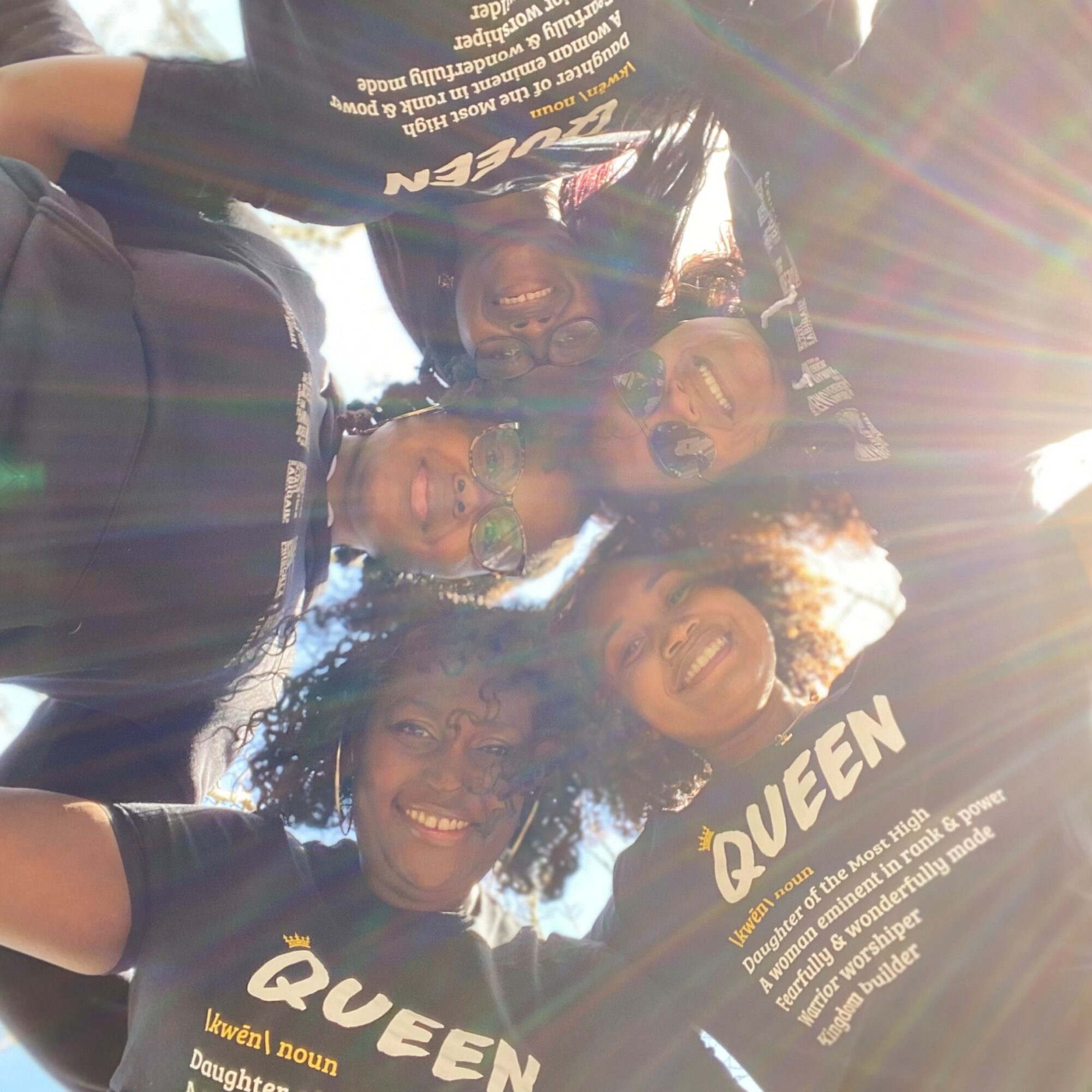 Group of five people smiling and looking down at the camera, sunlight shining brightly, creating lens flare effects.