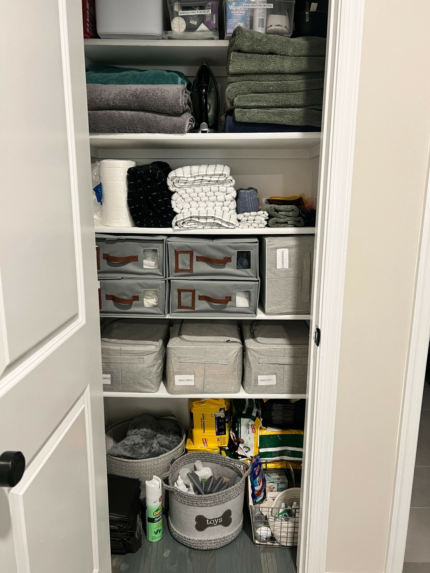 Closet with shelves containing storage boxes, towels, and toys, viewed from the front.