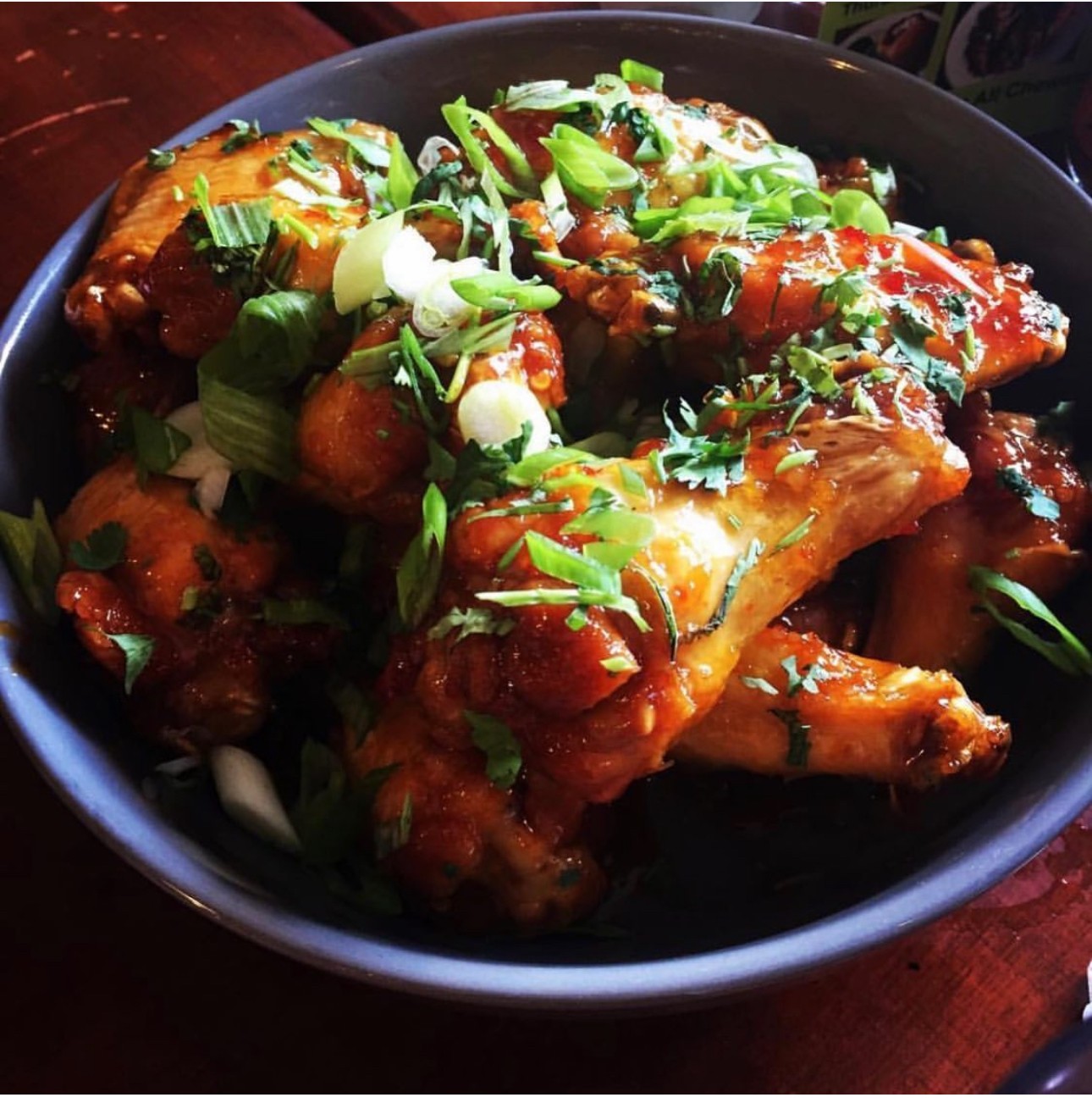 Bowl of chicken wings garnished with chopped green onions and herbs, served on a dark plate.
