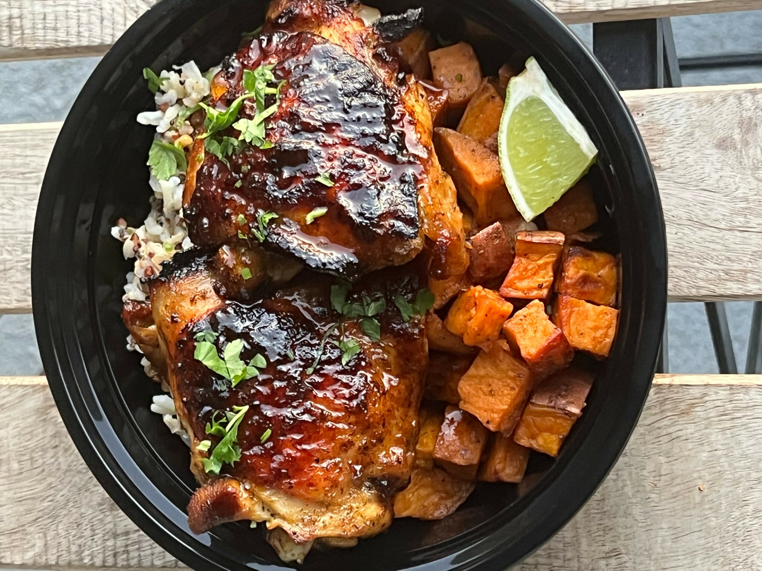 Barbecued chicken drumsticks with sauce, served with roasted sweet potatoes and a lime wedge, garnished with herbs.