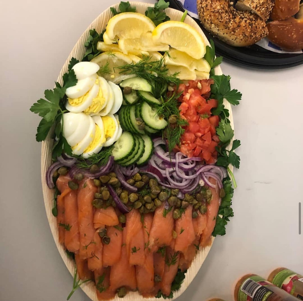 Assorted fresh vegetables including lemon slices, boiled eggs, cucumber, tomato, red onion, capers, and smoked salmon on a platter.