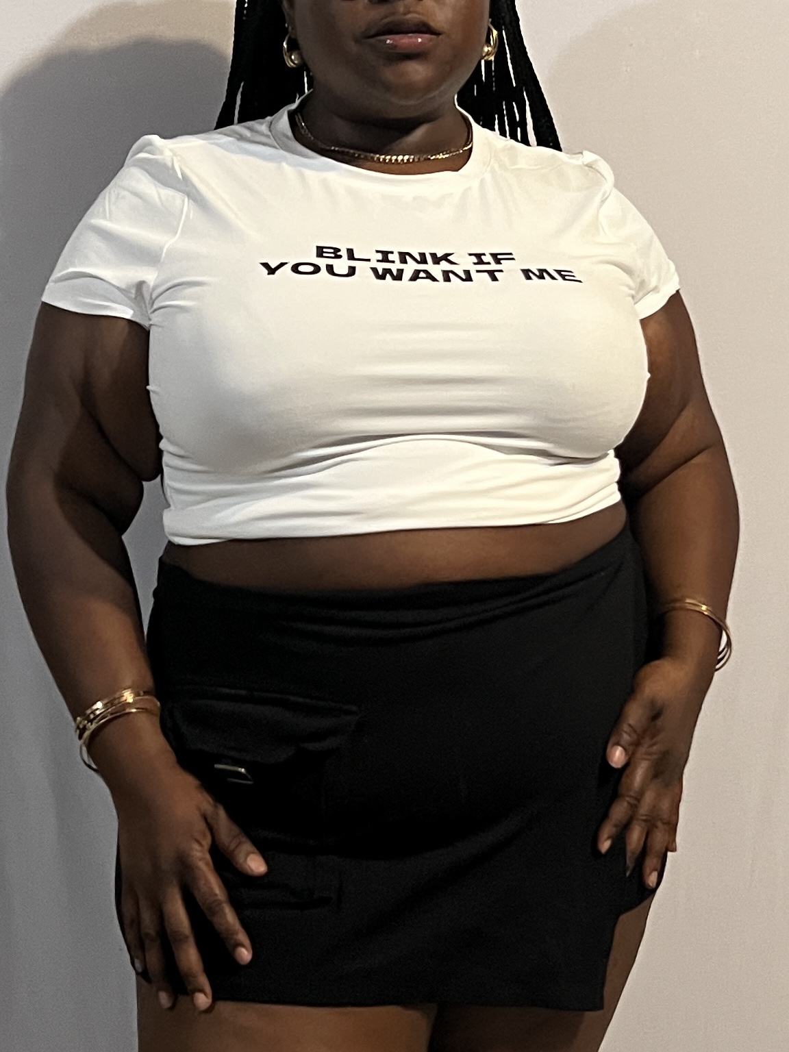 Person wearing a white T-shirt with text and a black skirt, standing against a plain background.