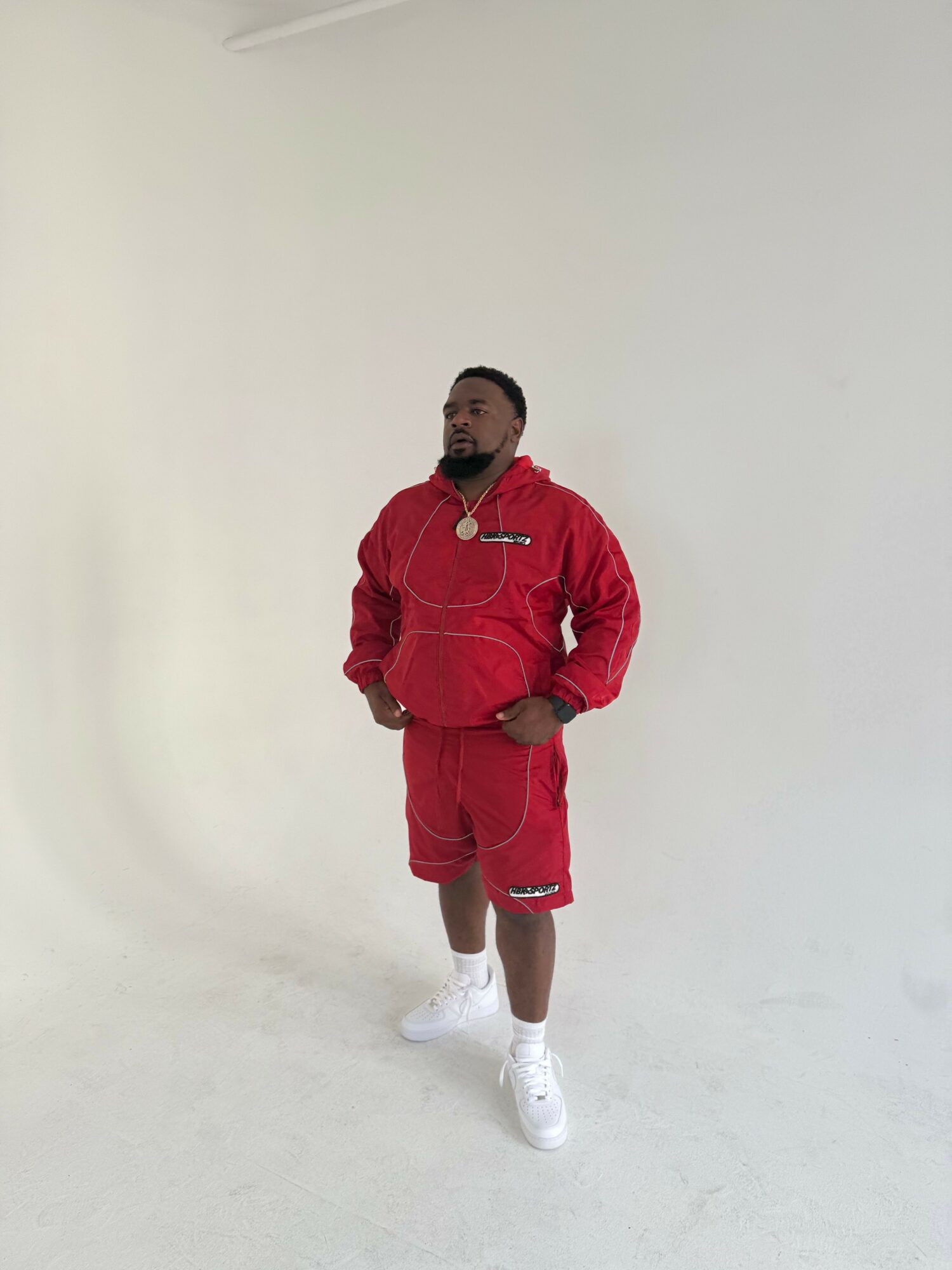 Person in red outfit standing against a plain white background, facing forward with hands in pockets, wearing white shoes.