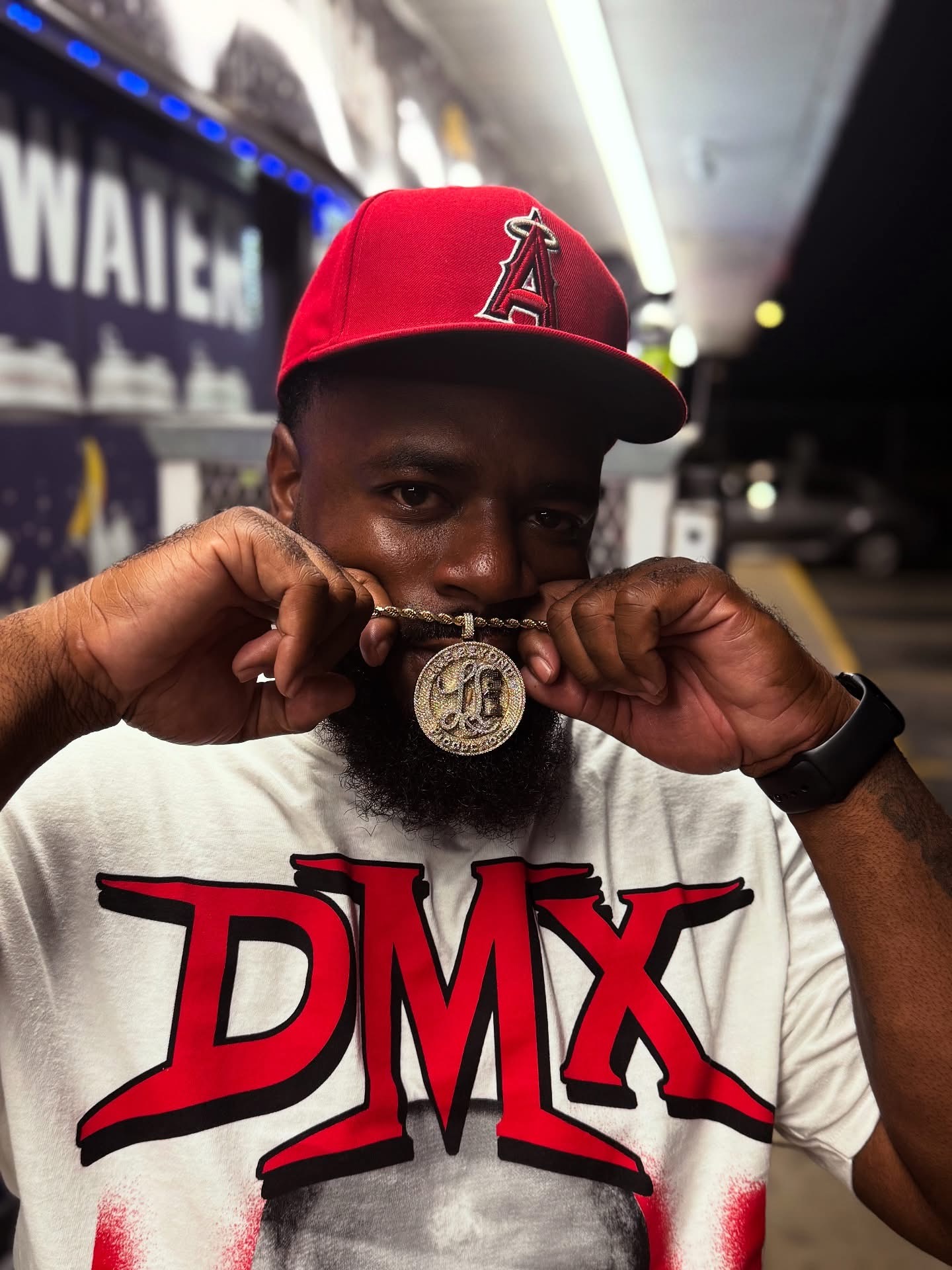 Man wearing a red cap and white T-shirt with red and black lettering, holding a medal in front of his face.