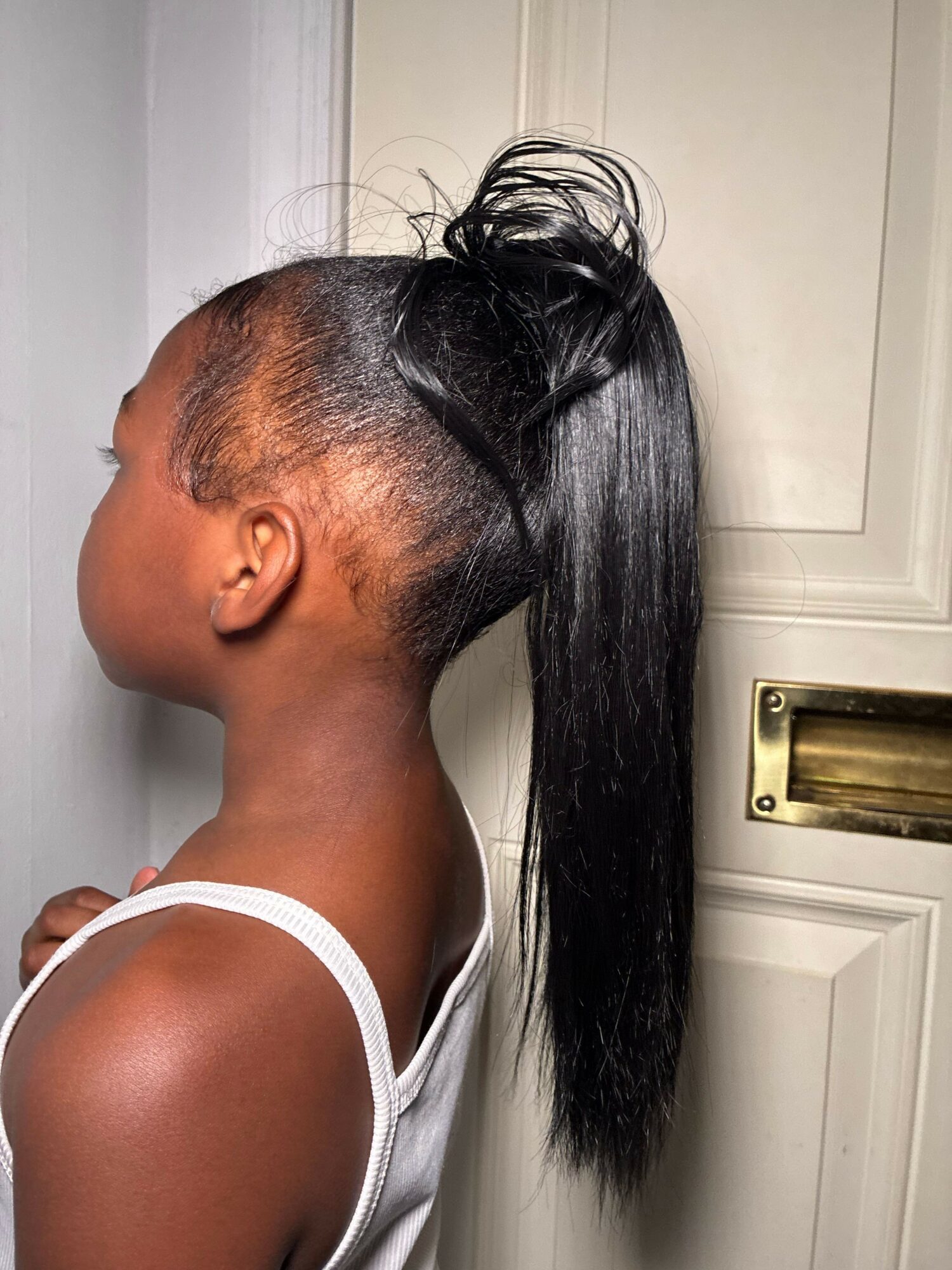 Side view of a woman with a high ponytail, wearing a white tank top, leaning forward. Word count: 20.