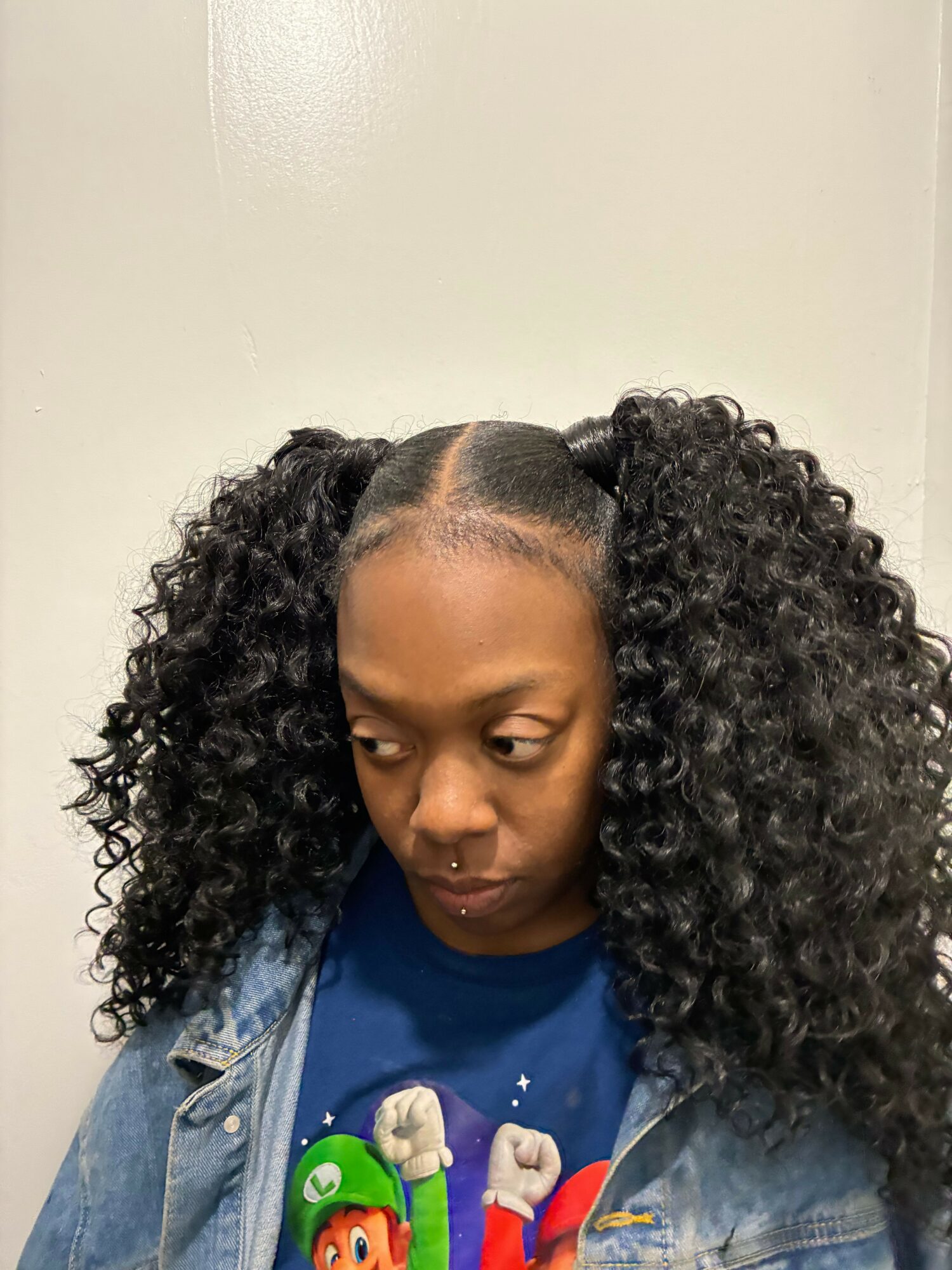 Woman with curly hair and a denim jacket, looking down, against a plain background.