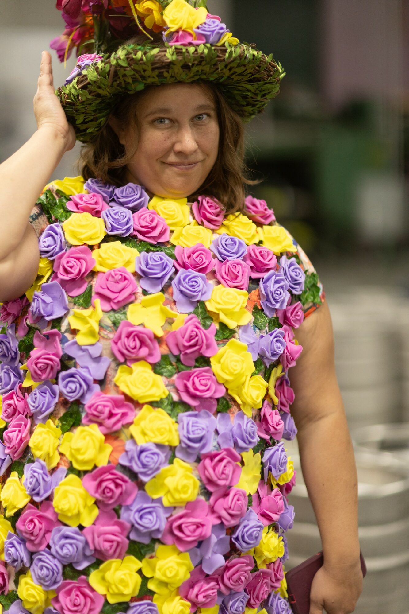 Woman wearing a hat and dress made of colorful roses, smiling outdoors.