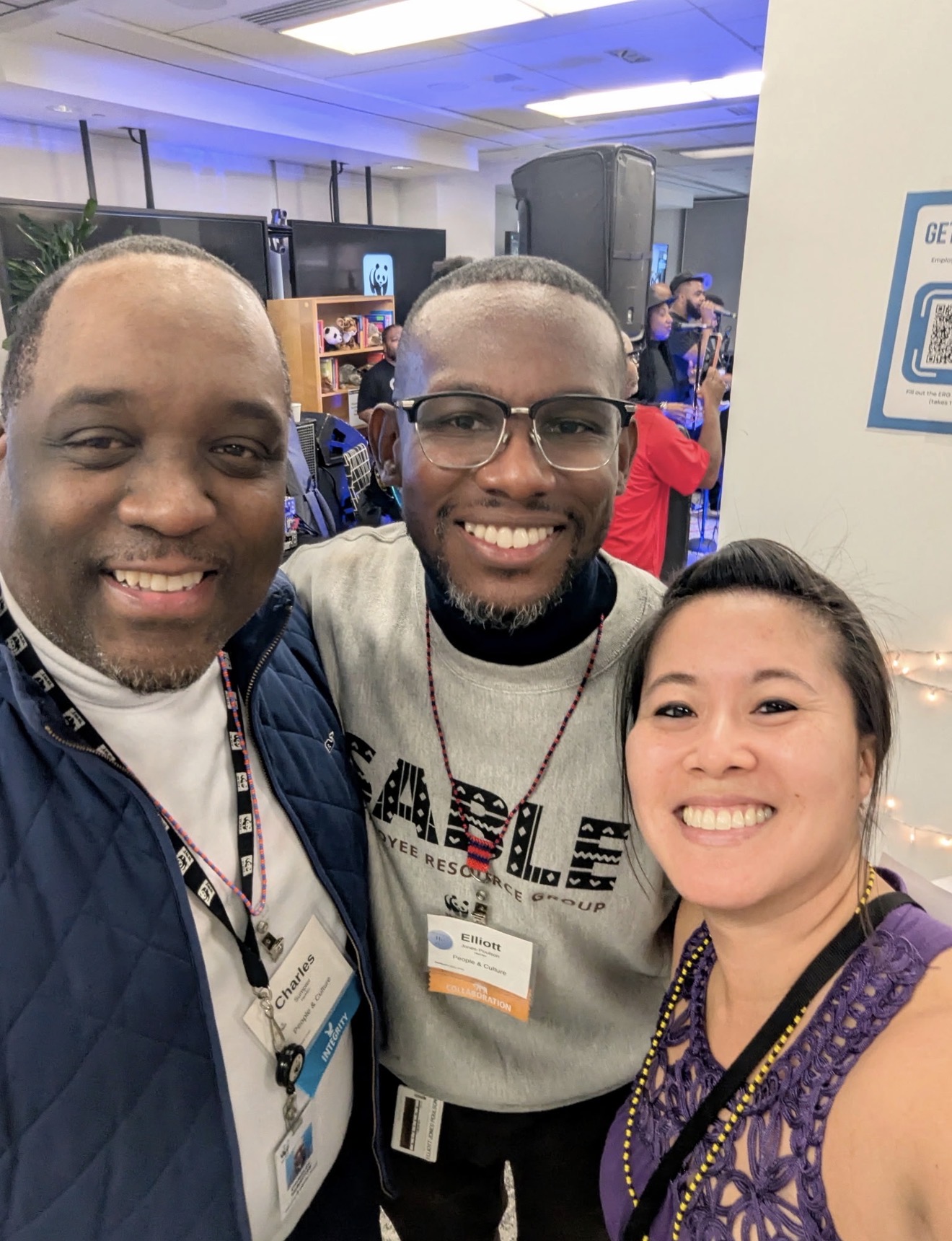 Three people smiling and posing for a photo at an indoor event, with a background of booths and people.