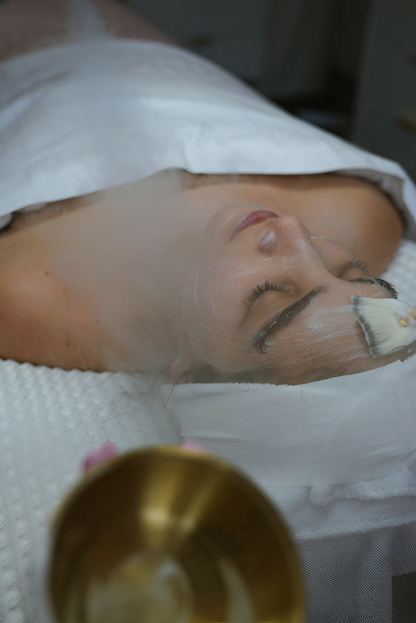 Person lying in hospital bed with bandage on head, eyes closed, and a white pillow, viewed from the side.
