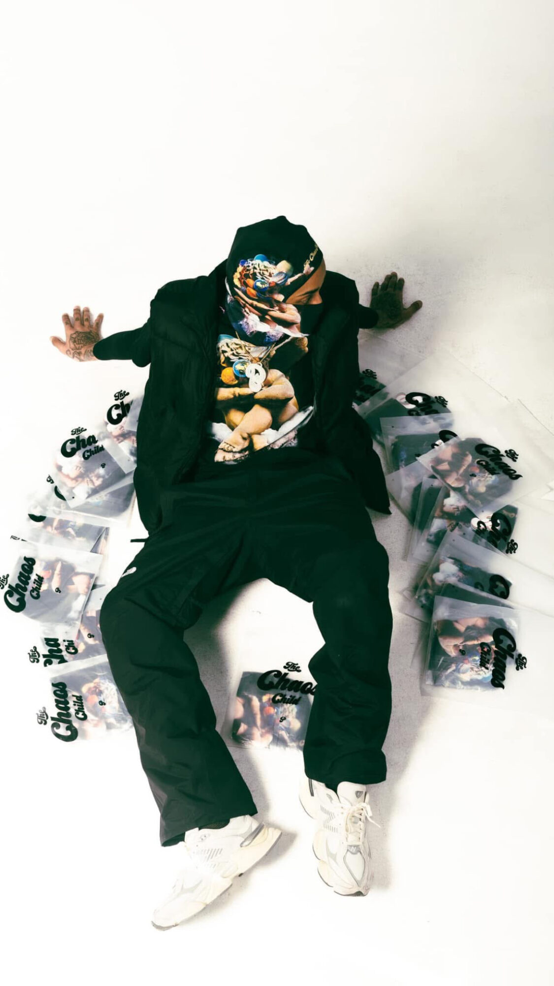 Person sitting on the floor surrounded by plastic bags and toys, holding a phone, with a plain white background.