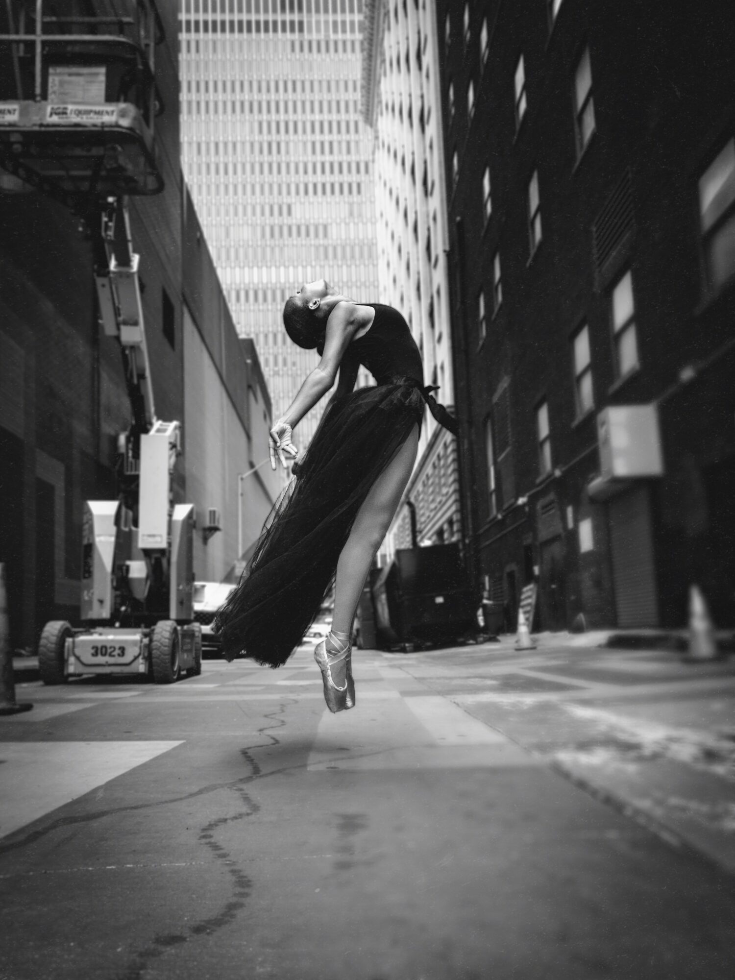 Ballet dancer in a city street, balancing on toes with a long flowing skirt, tall buildings in background.