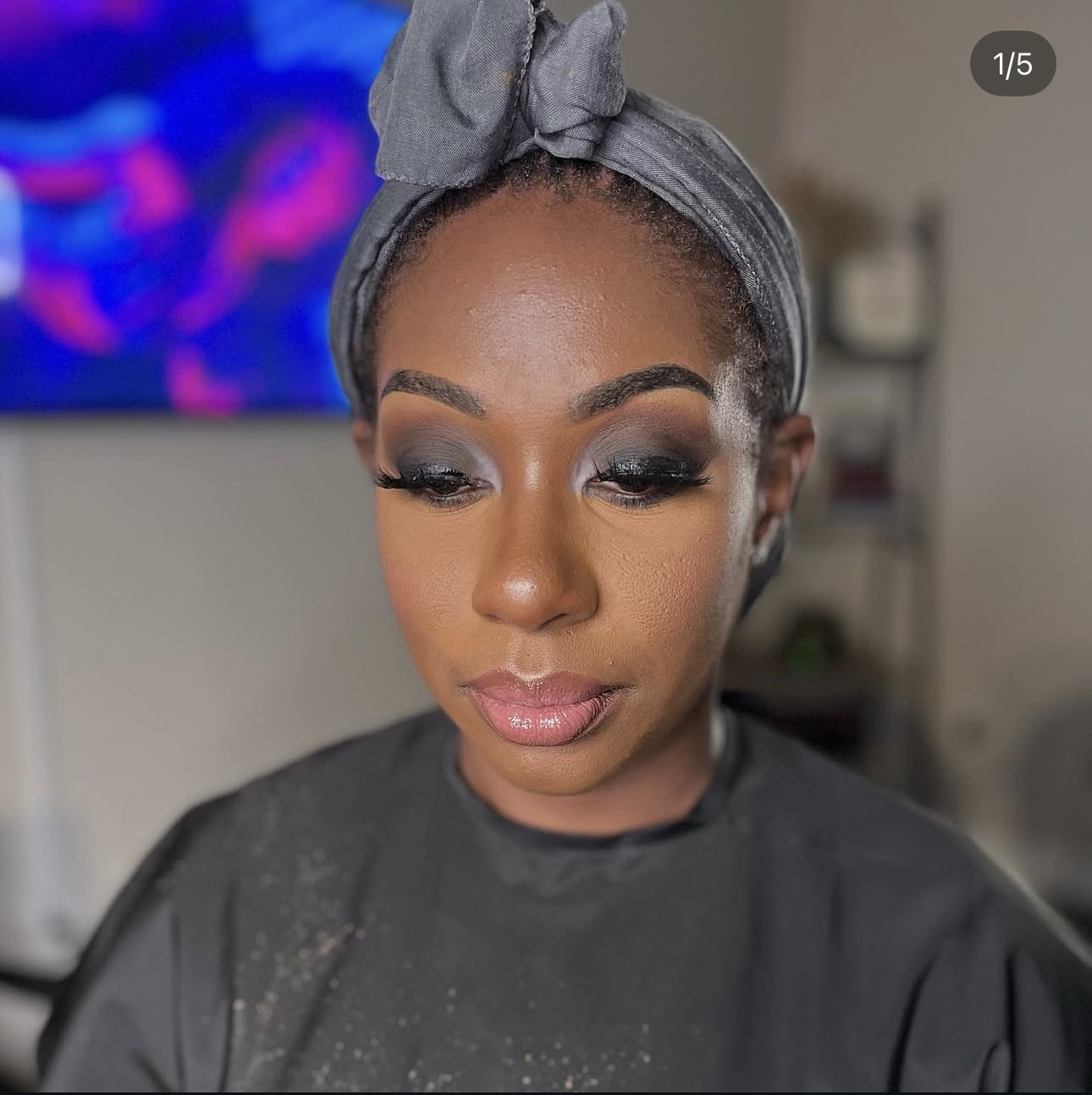 Close-up of a woman with makeup and a gray headband, looking downward, indoors.